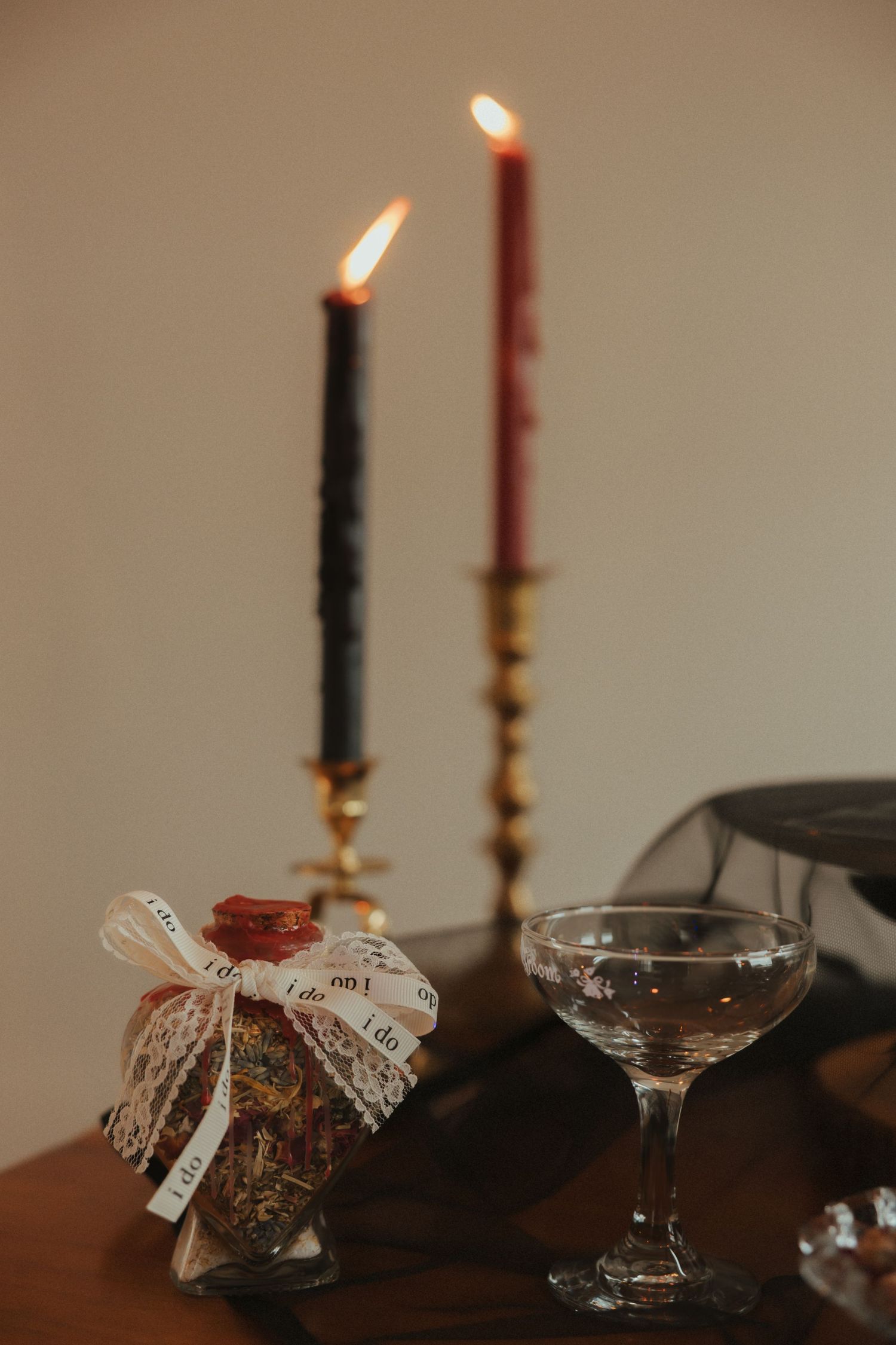 Romantic candlelit setting with two lit candles in brass holders, decorative jar with lace ribbon, and coupe champagne glass.