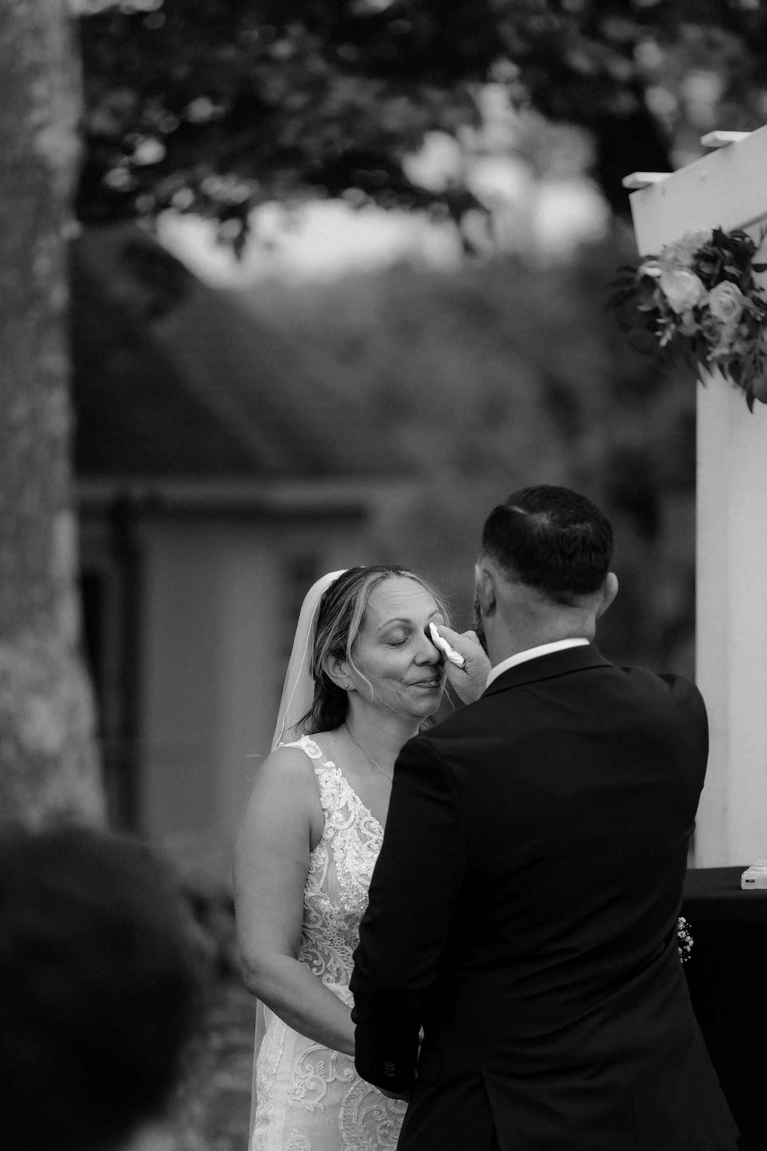 A romantic black and white wedding photograph showing a couple embracing during their outdoor ceremony.