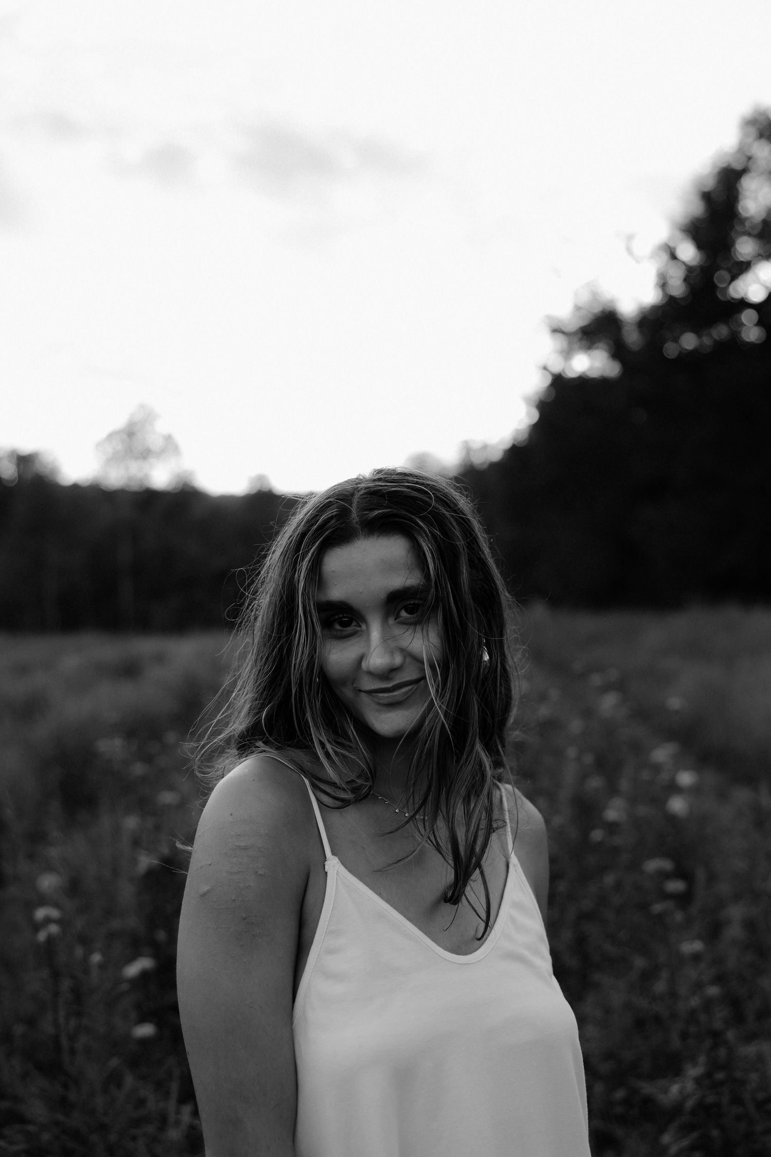 A series of black and white portraits showing someone in a white sleeveless top against a natural outdoor background.