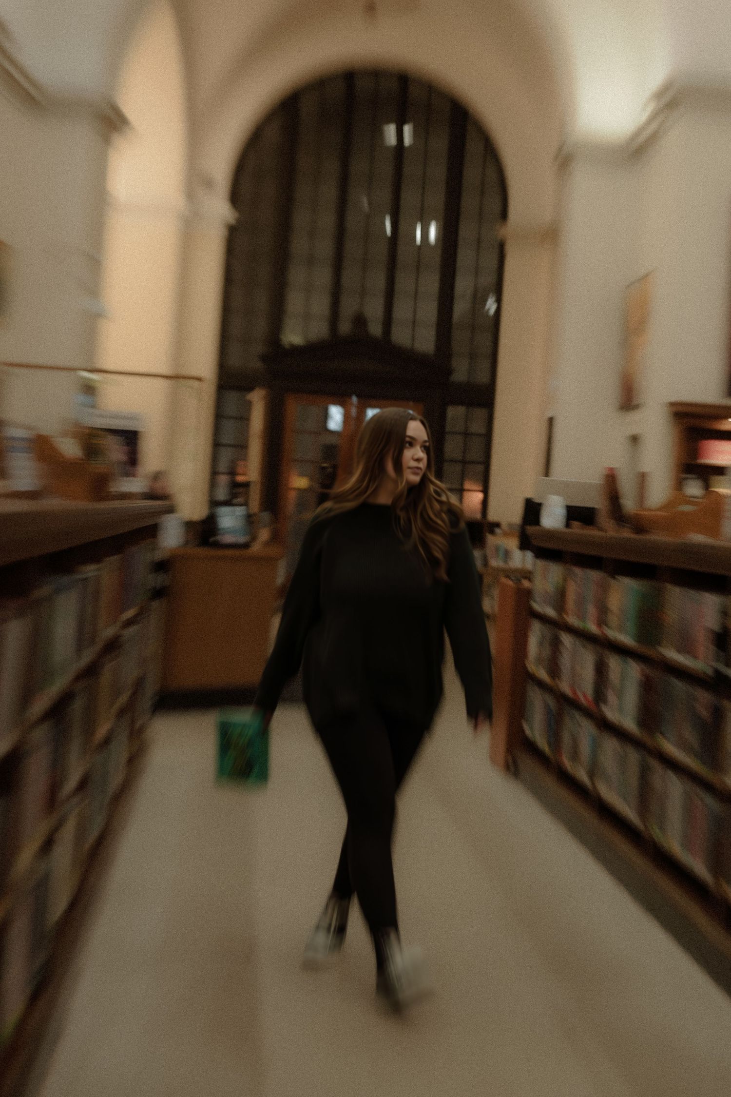 A person in dark clothing walks through library stacks in a motion-blurred atmospheric shot.