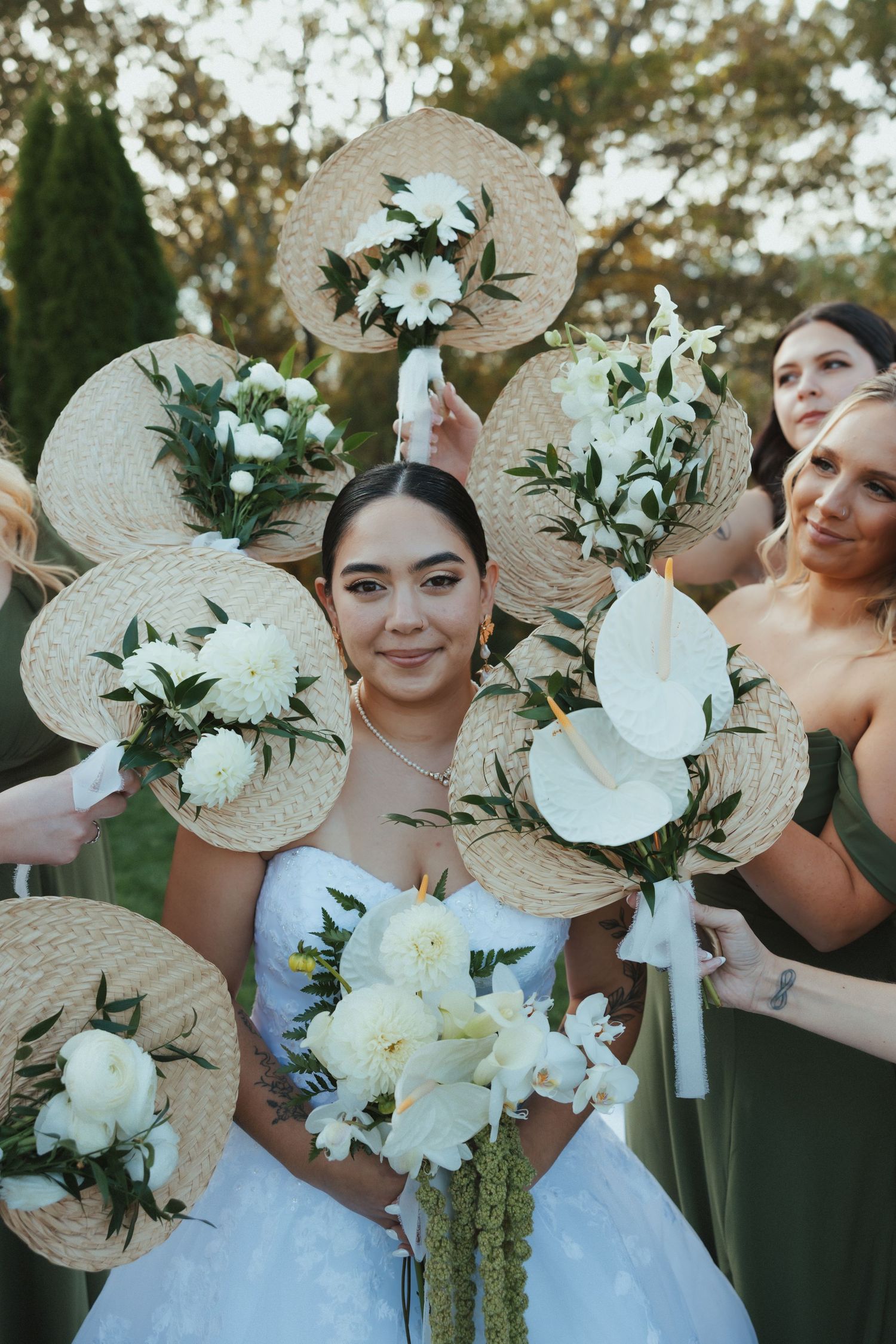 Wedding party holding decorative straw fans adorned with white flowers and greenery at an outdoor celebration.