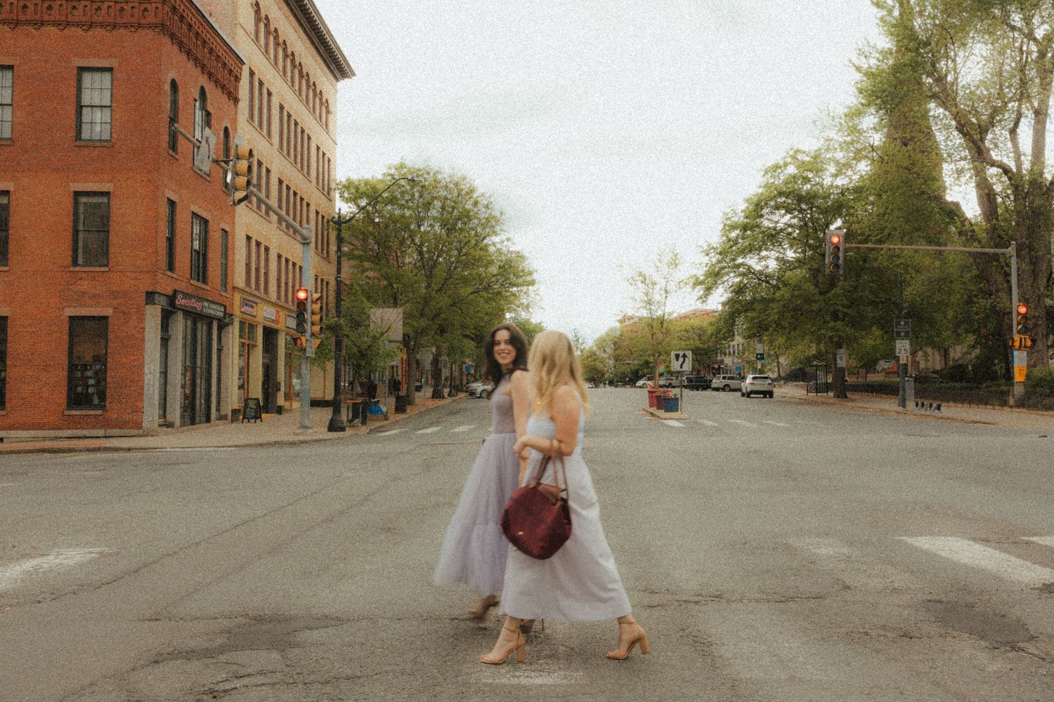 Someone in a flowy white dress stands in the middle of a quiet brick-lined street in a historic neighborhood.