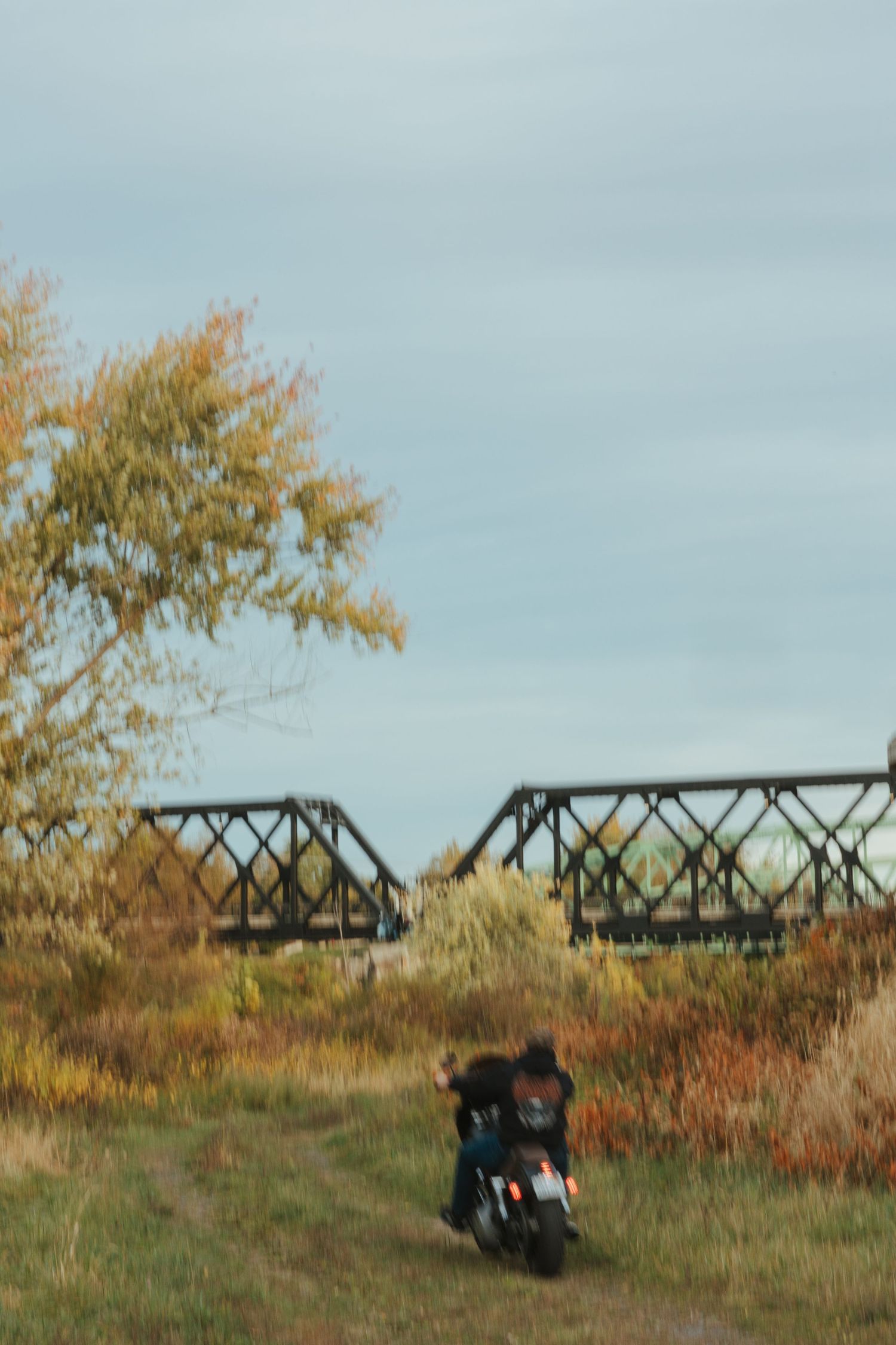 A black motorcycle parked on a grassy hill with an industrial bridge structure visible in the background.