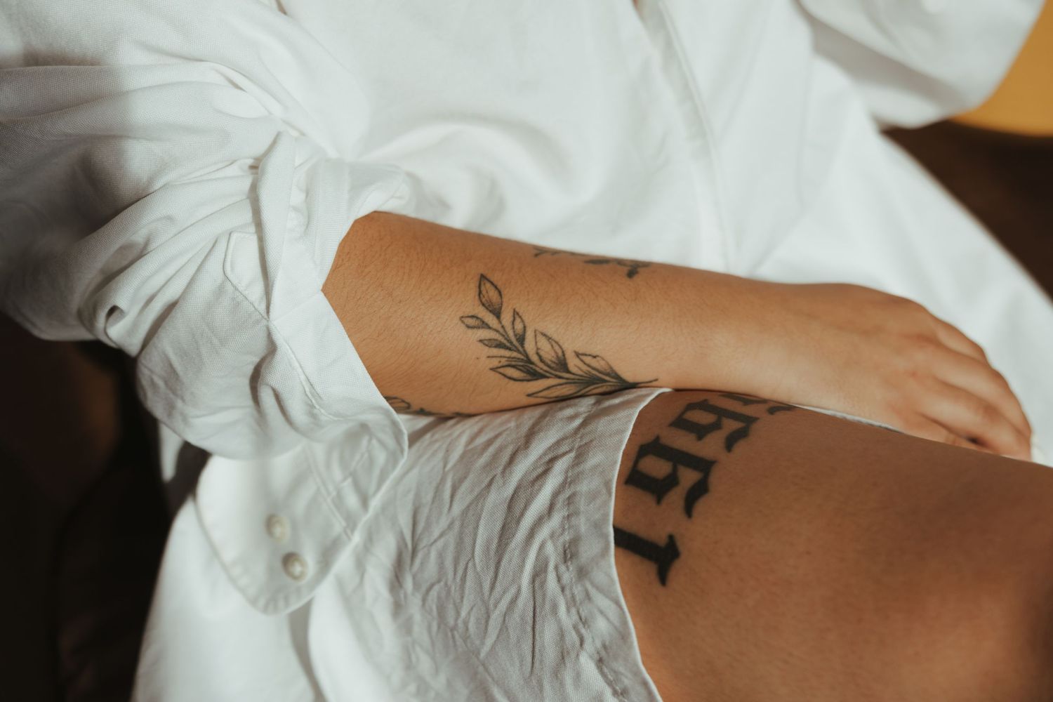 Close-up of a delicate leaf tattoo design on someone's forearm against white fabric background.
