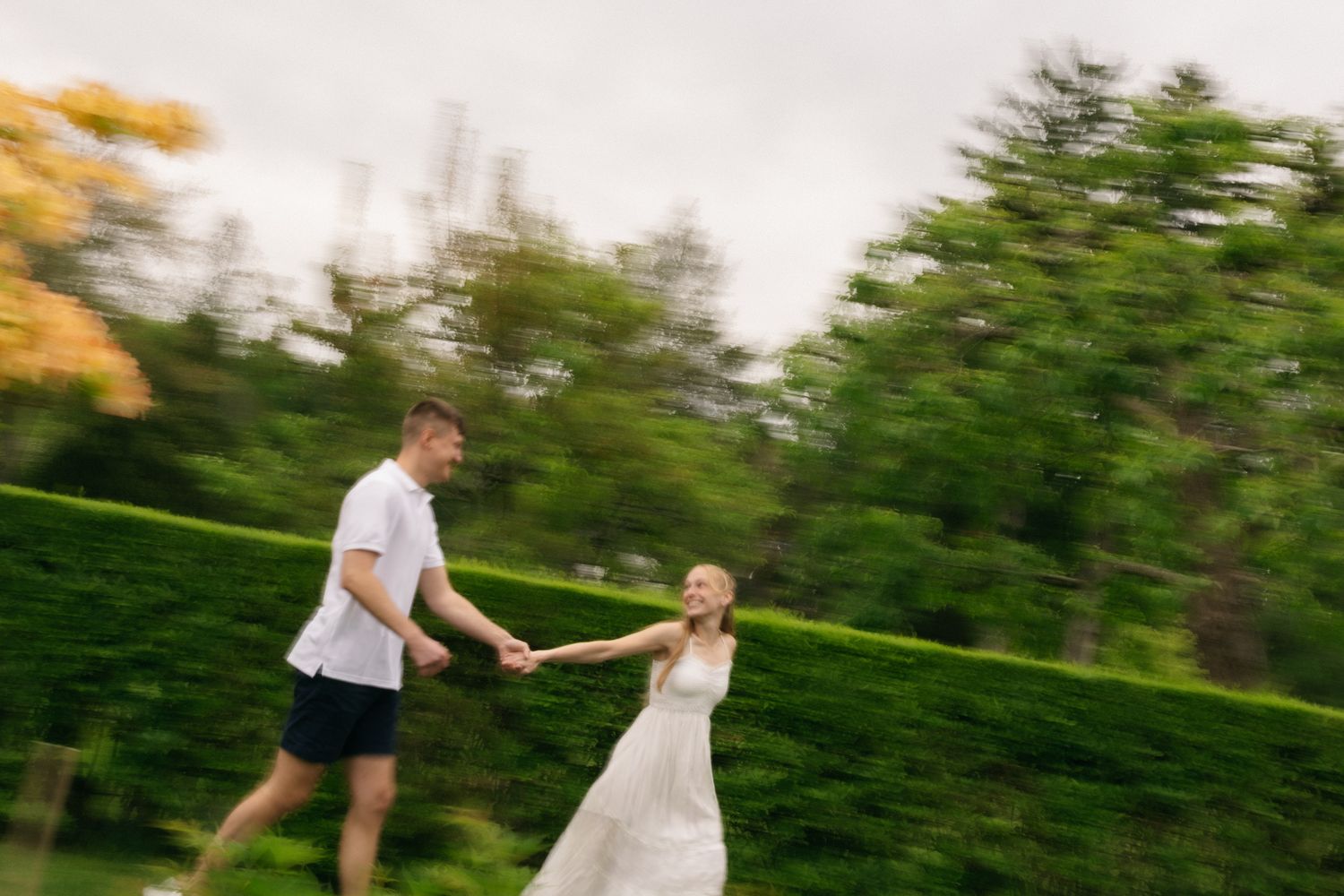 A couple runs hand-in-hand through a lush green park, the bride in a white dress, groom in casual attire, motion blur adding romance.