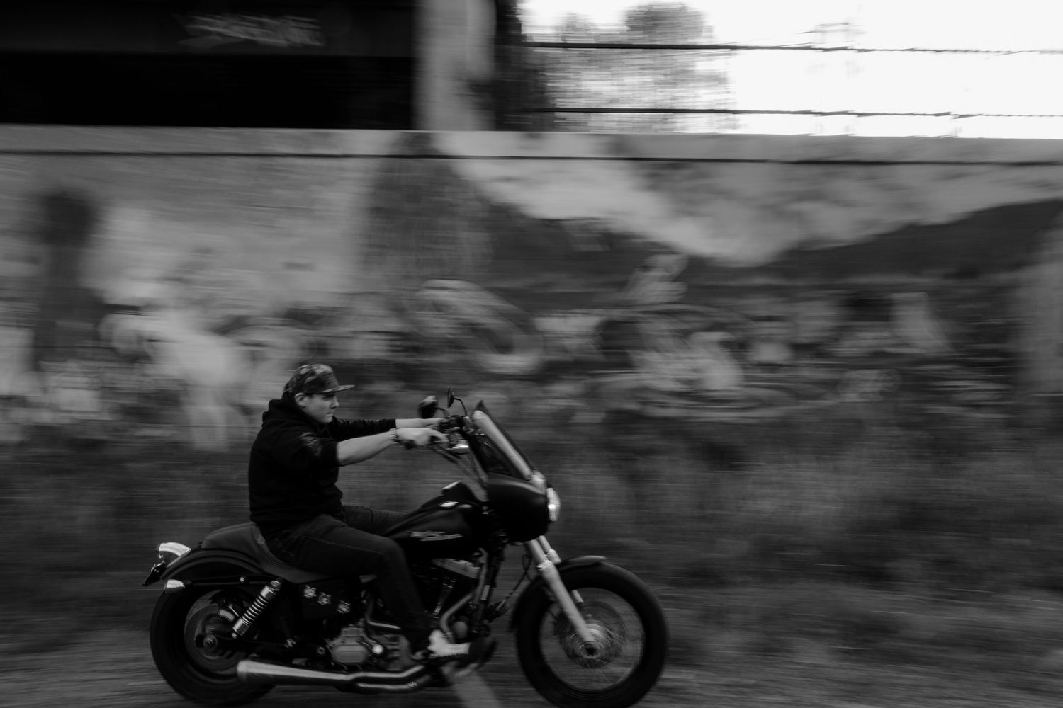 Black and white silhouette of a vintage motorcycle parked against a mountainous landscape backdrop.