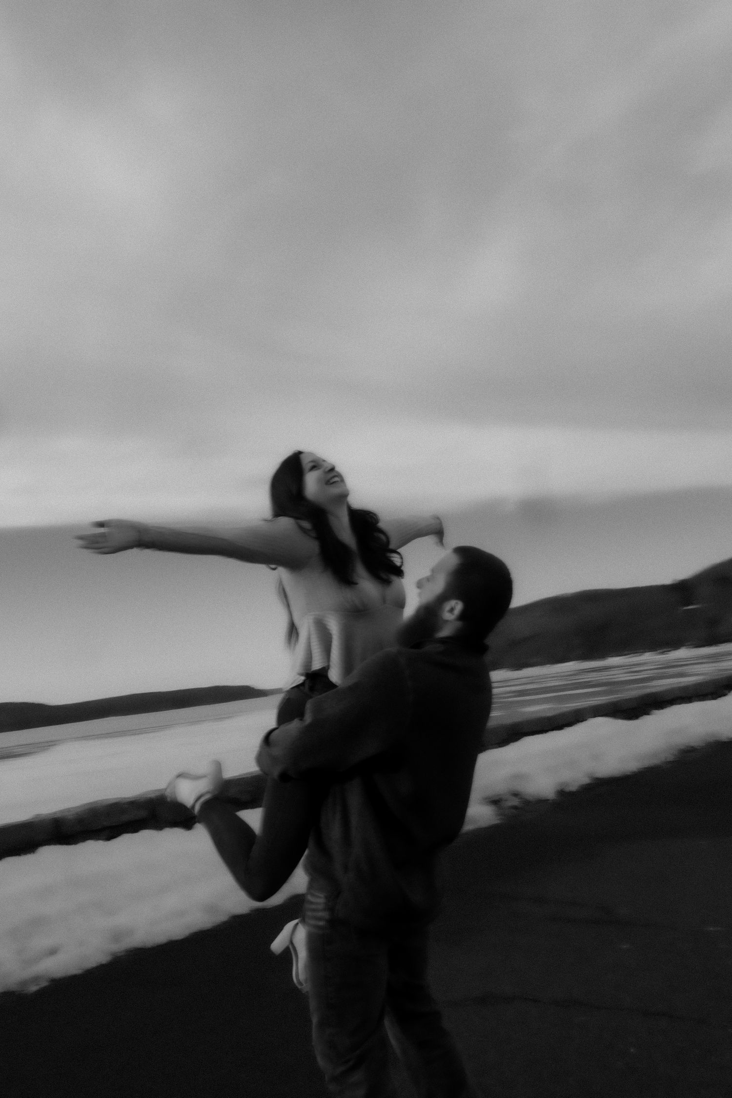 A black and white photo sequence shows two figures playfully dancing together on a hillside against a cloudy sky.
