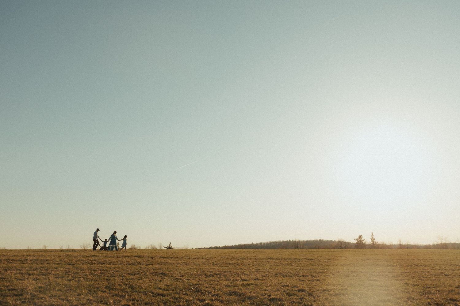 Silhouettes of people walking along a hilltop horizon against a warm sunset sky.