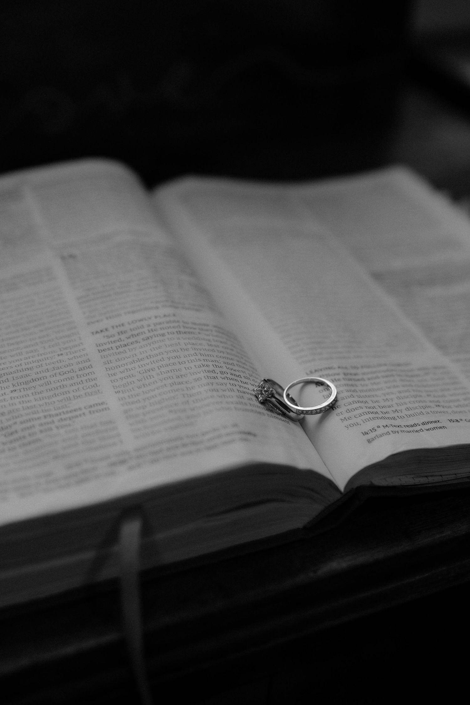 A silver wedding ring rests on the open pages of a book in black and white photography.