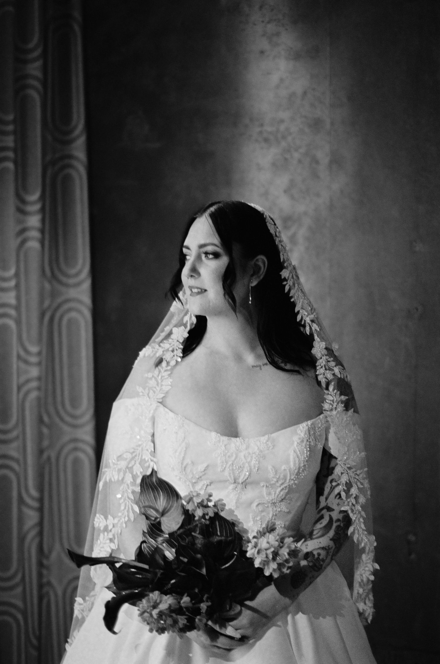 Black and white bridal portrait of a woman in lace wedding dress and veil holding a bouquet.
