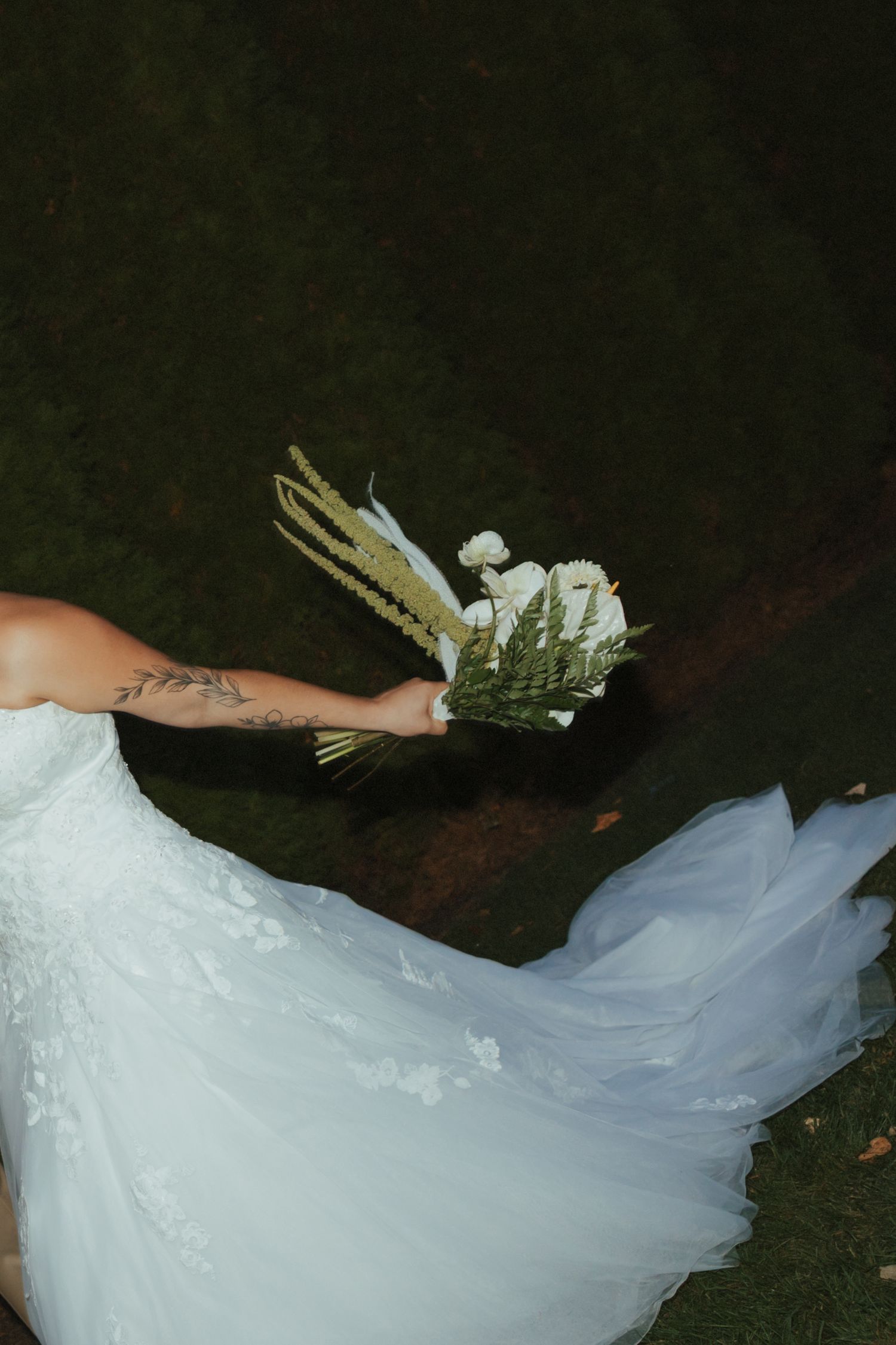 A flowing white wedding dress train with lace details trails across dark grass in a series of artistic photos.