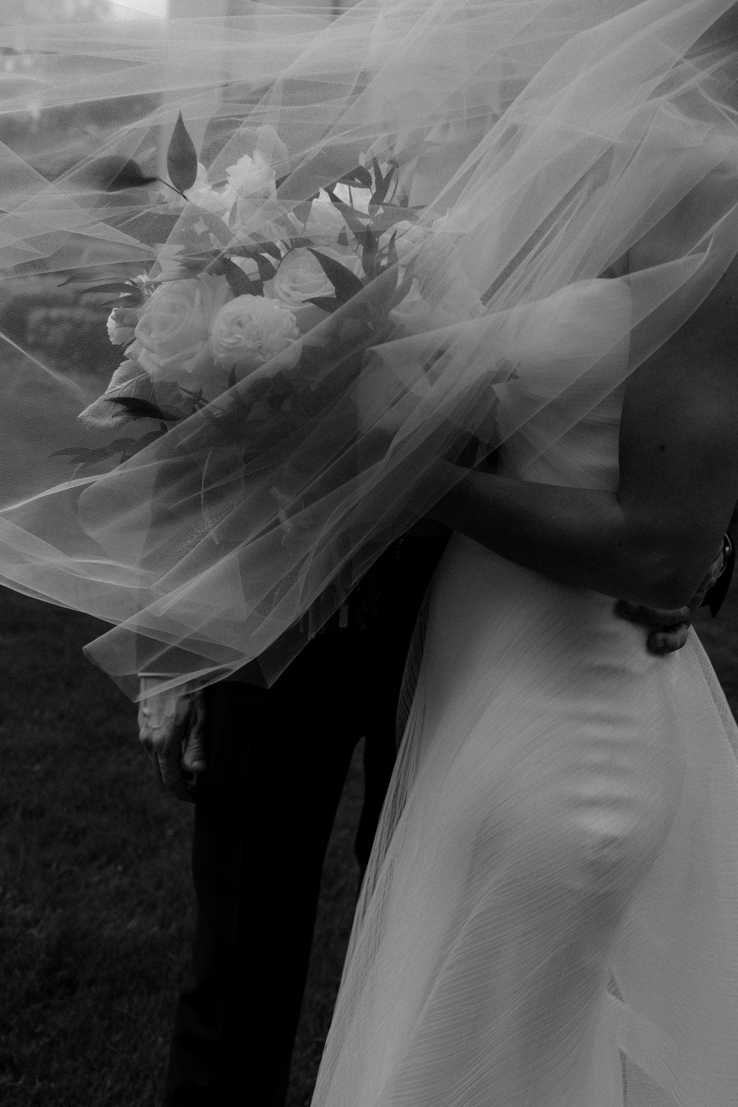 A black and white artistic wedding photo showing delicate tulle veil details with soft floral accents.