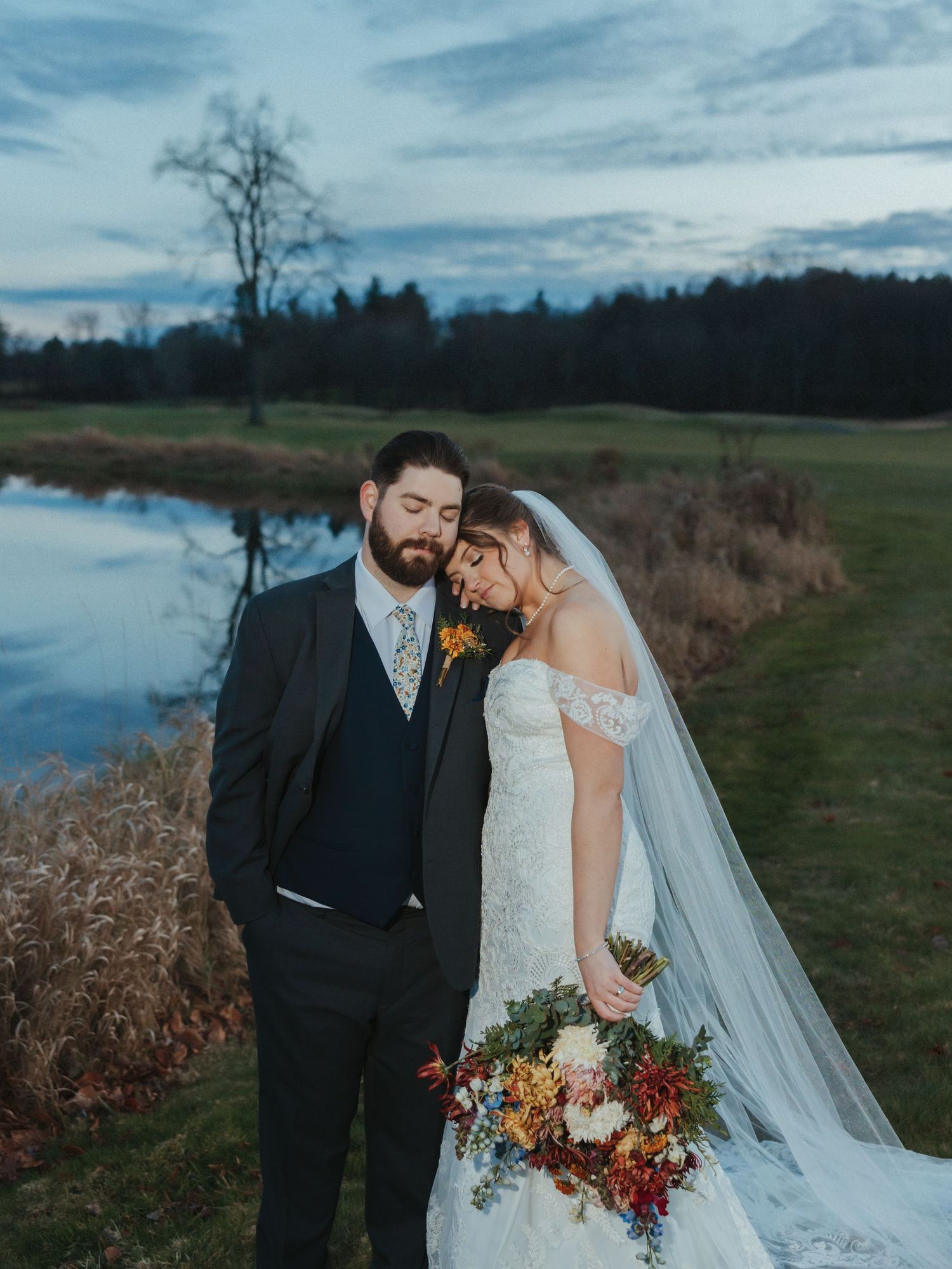 Newlyweds share intimate moments during sunset in a rustic outdoor setting with dramatic cloudy skies and autumn foliage.