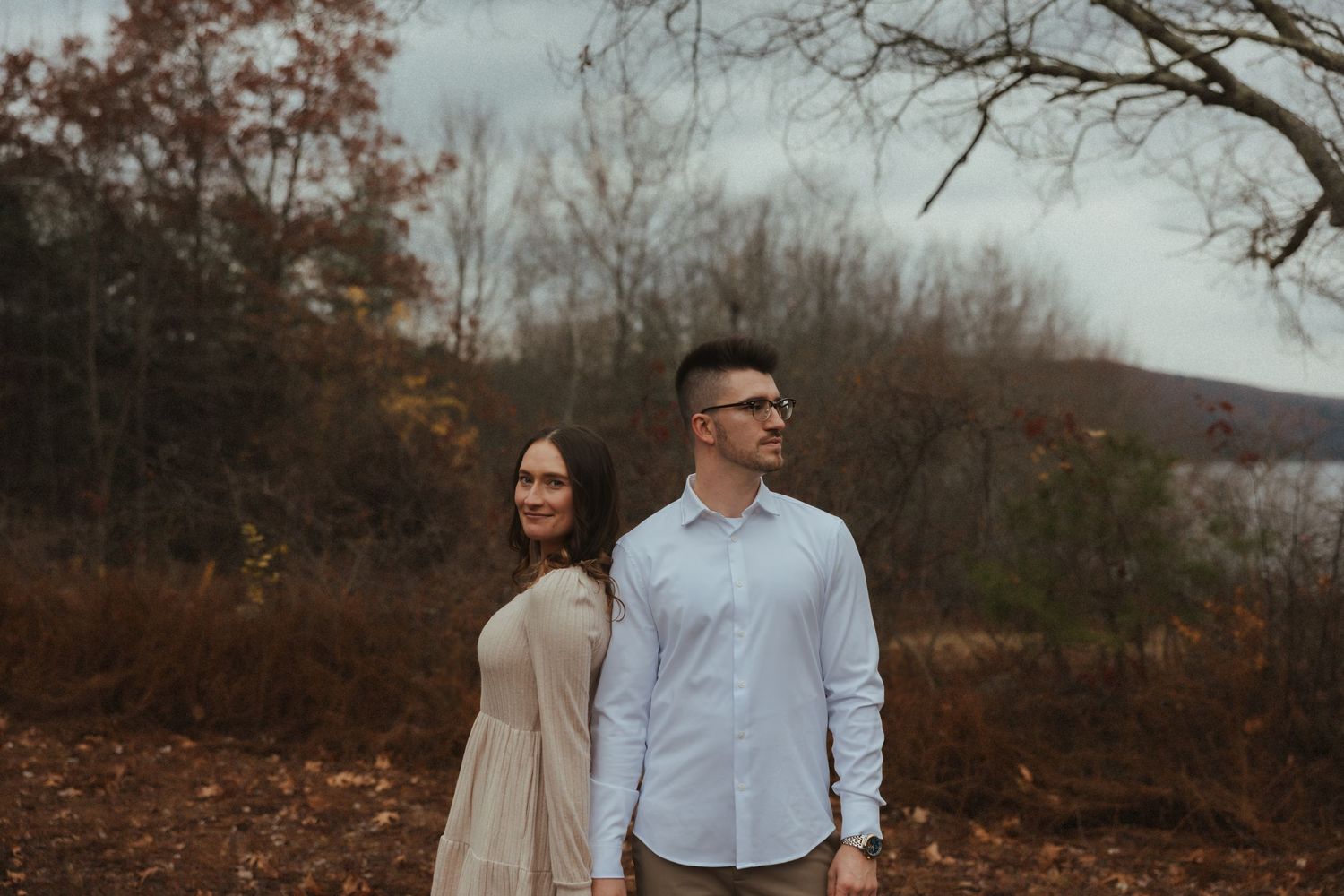 Romantic couple walking together through an autumn forest with bare trees and fallen leaves at sunset.