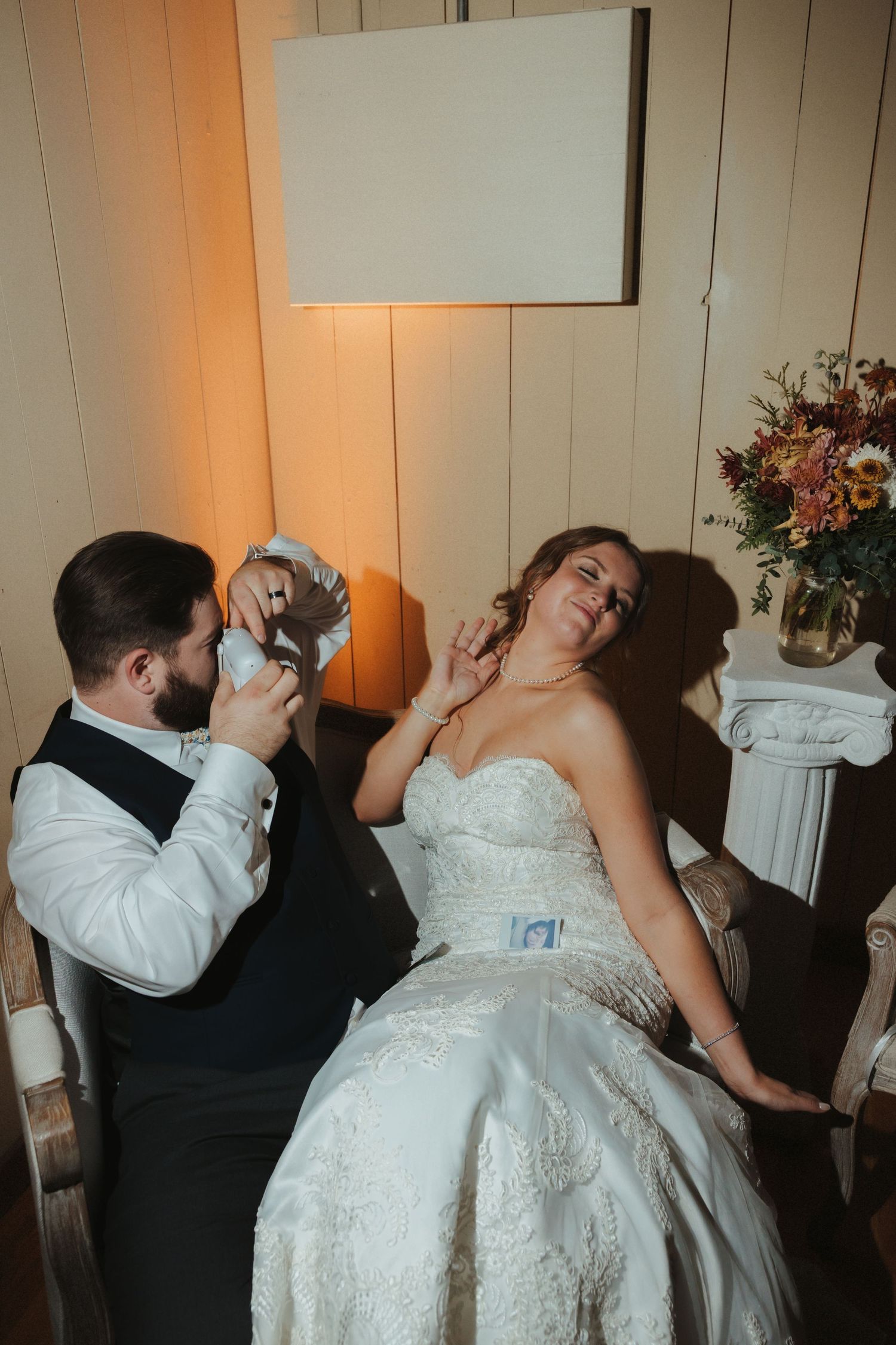 Wedding couple shares a playful dip dance moment in a rustic indoor venue with white walls.