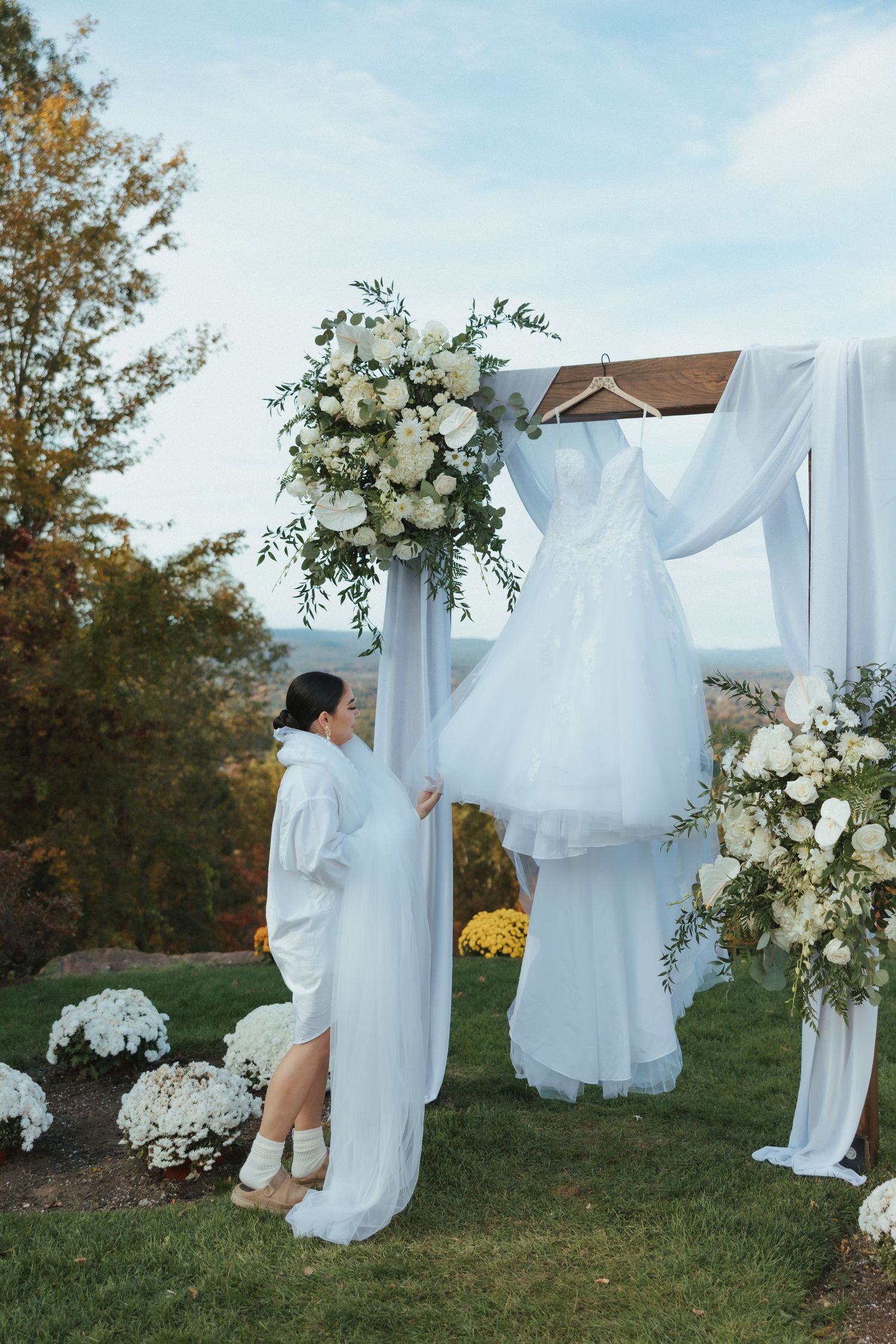 White fabric and floral arrangements create an ethereal outdoor wedding backdrop against a natural autumn landscape.