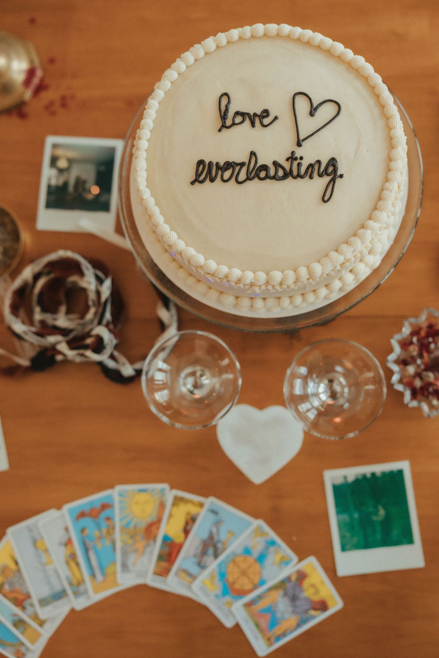 A series of white frosted cakes with handwritten messages displayed next to scattered tarot cards on a wooden table.