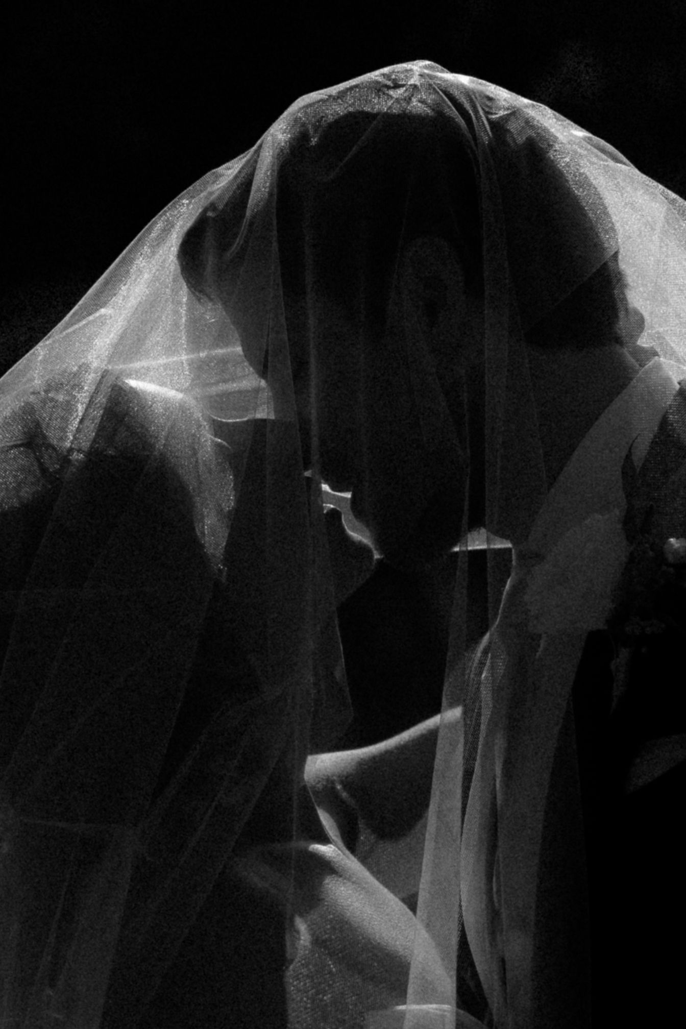 A delicate bridal veil flows gracefully in the air against a dark background creating a romantic silhouette.