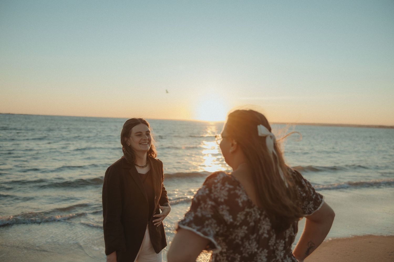 Two people enjoy a tranquil sunset moment on the beach with golden sunlight reflecting off the ocean waves.