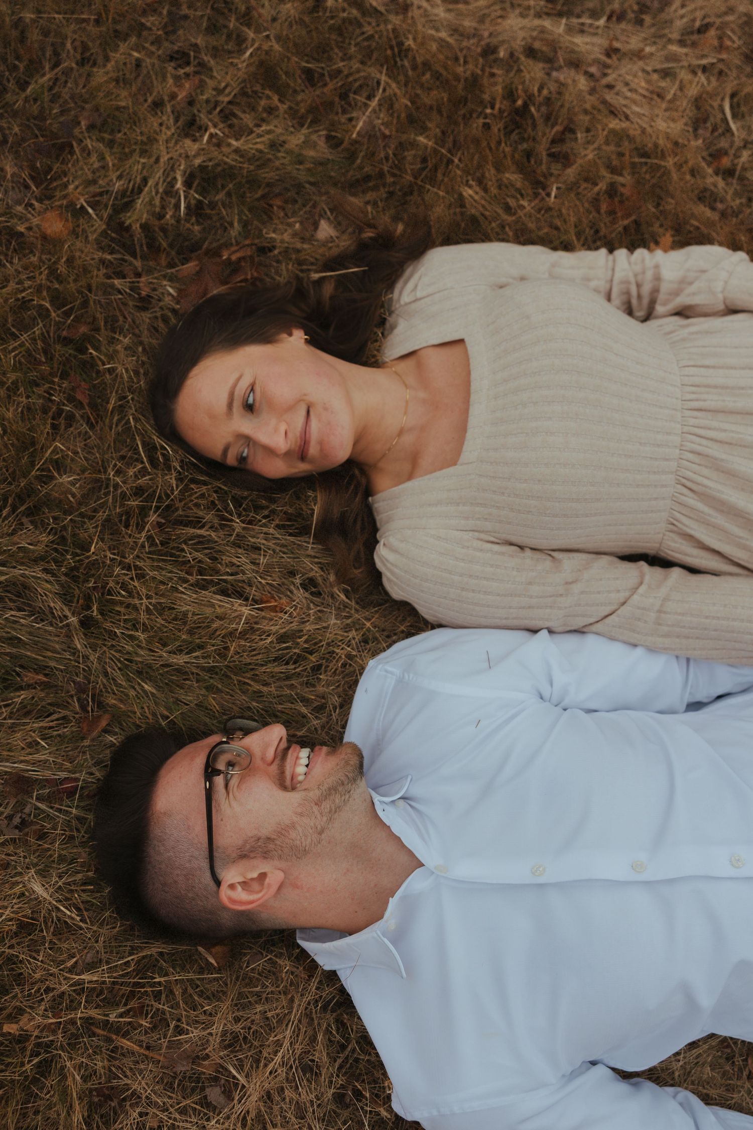 A couple lying on dried grass looking relaxed and content during an outdoor photo session.