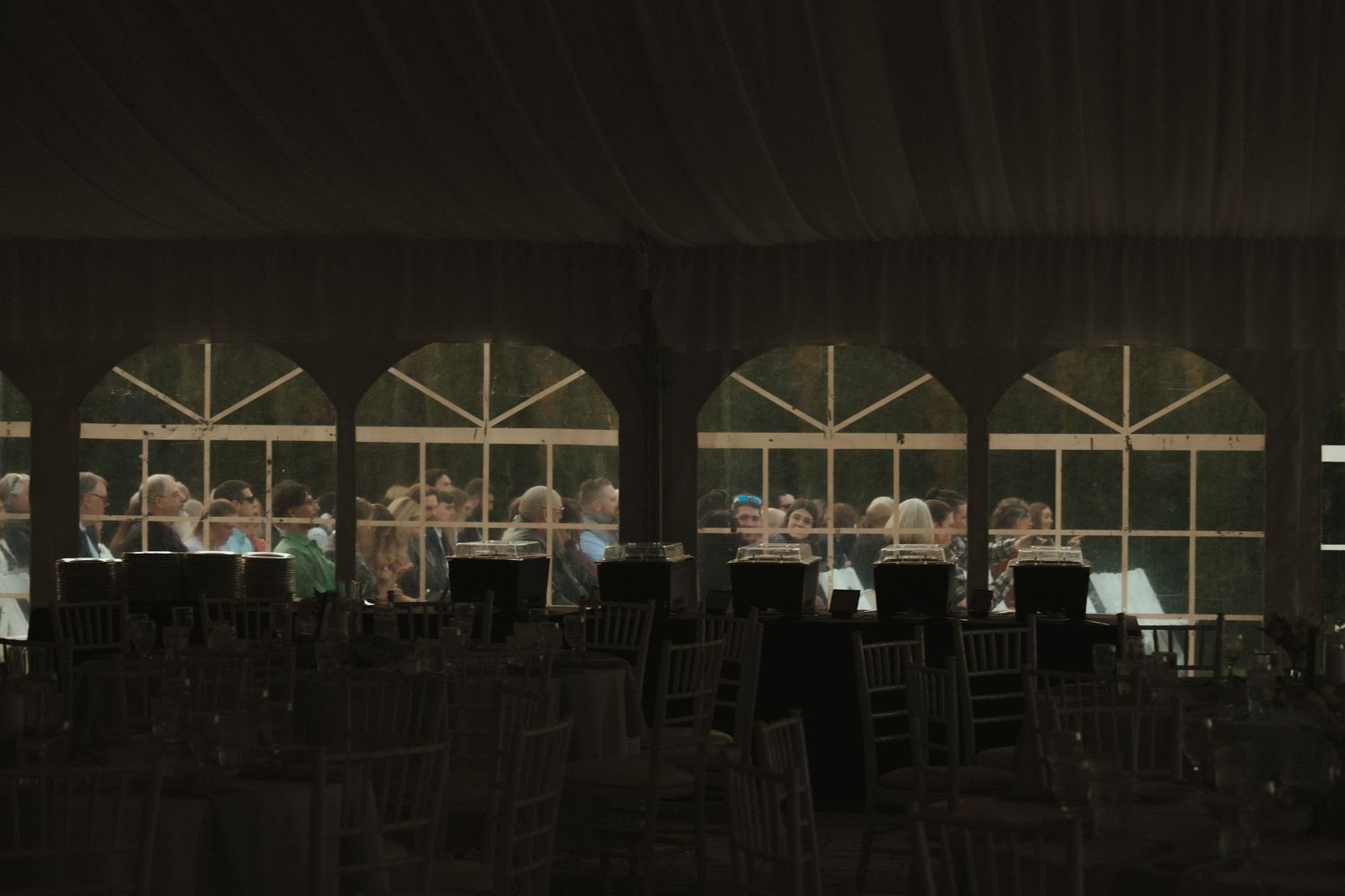Dark silhouettes of chairs and tables inside an illuminated tent with arched windows at night.