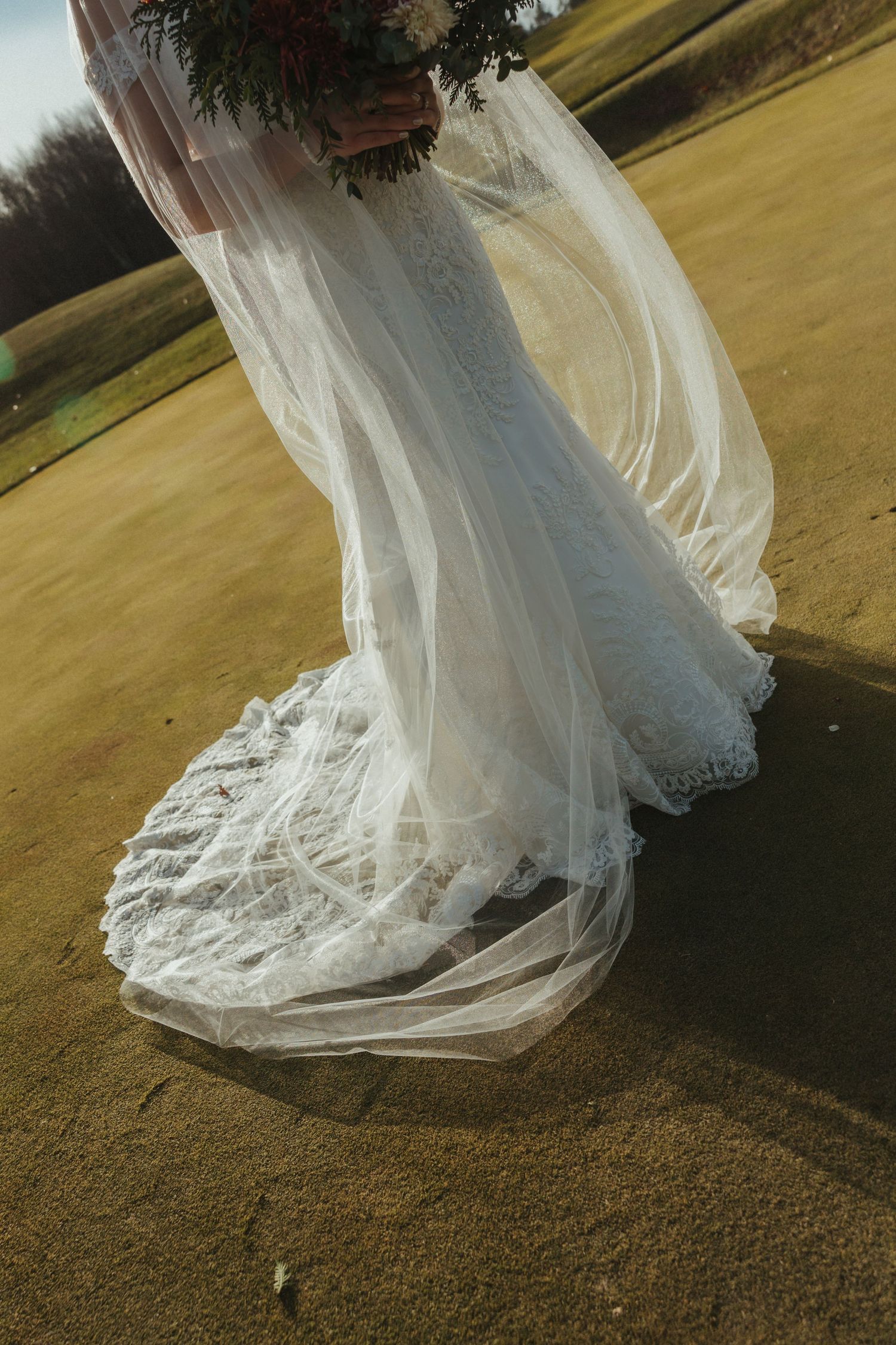 A flowing white wedding dress train with delicate lace details swirls gracefully on sandy ground.