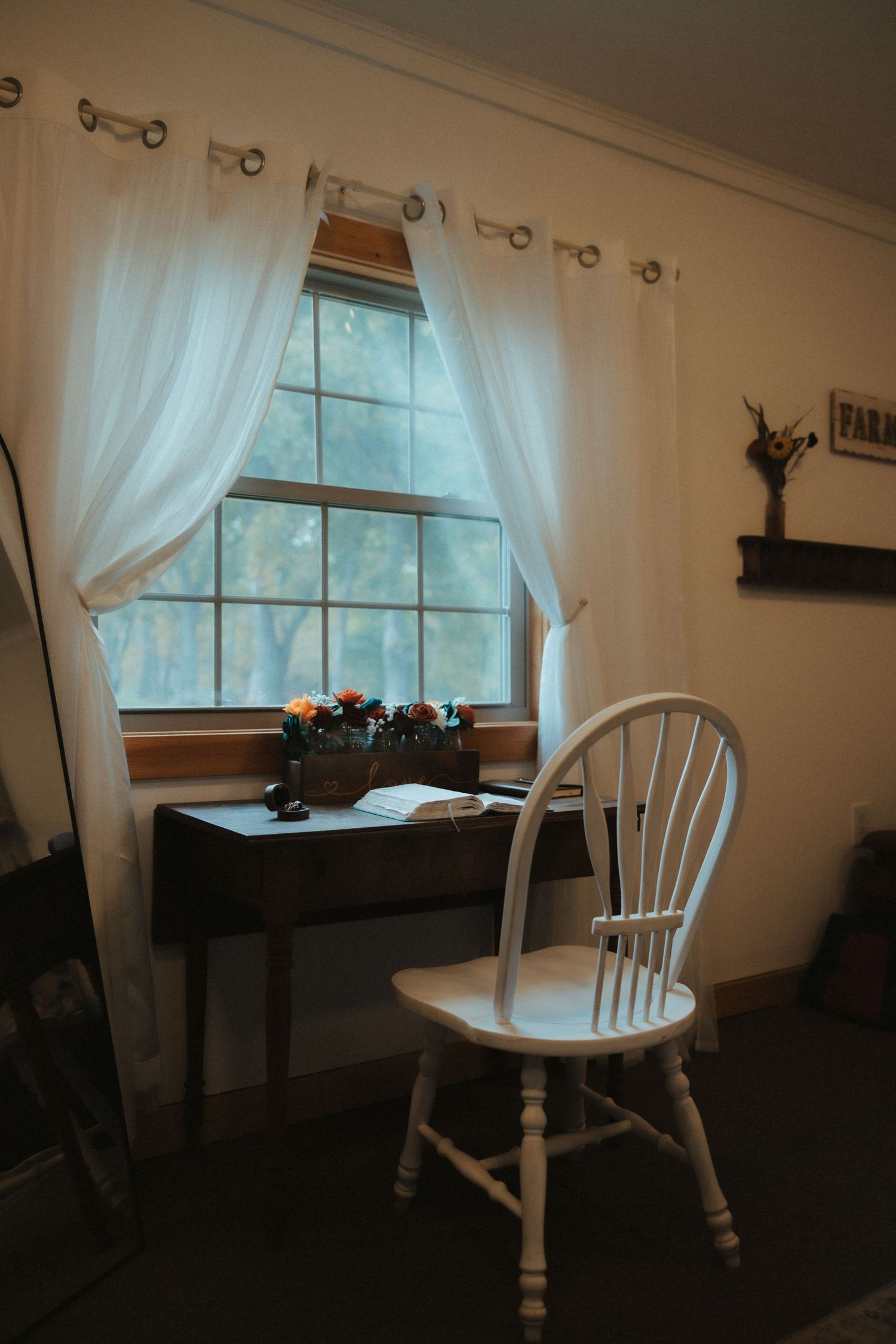 A rustic dining area with white curtains, wooden chairs and natural light streaming through windows.