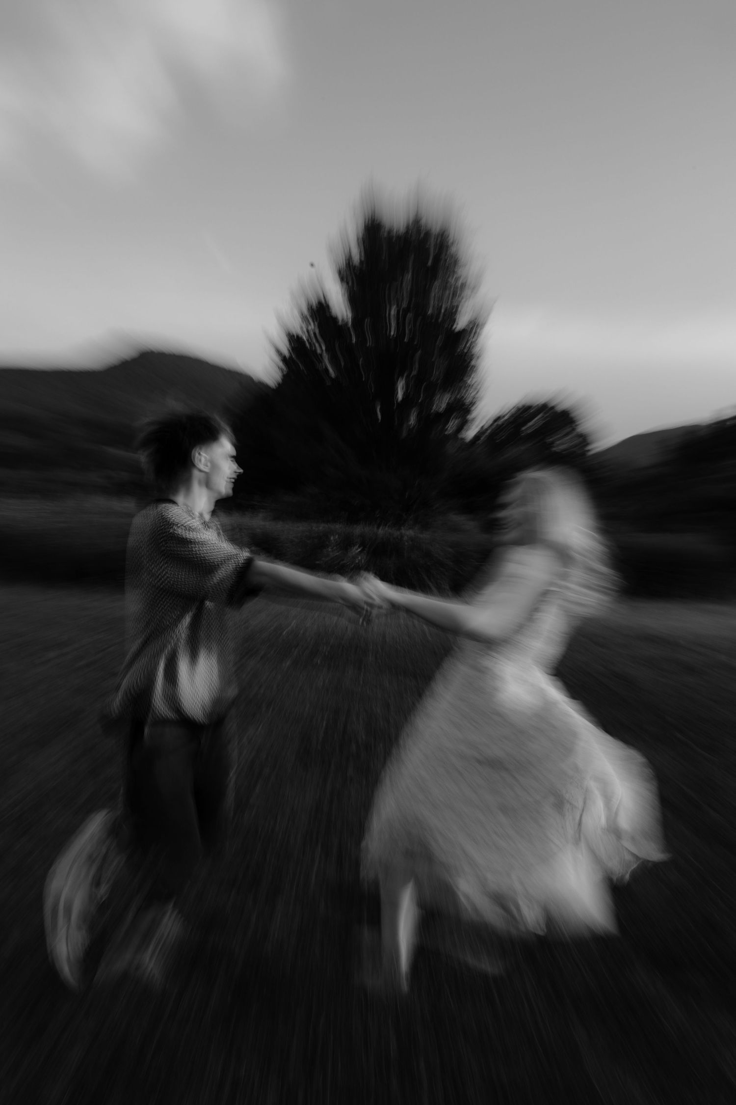 A blurred black and white sequence of two people in motion showing a dramatic spinning movement outdoors.