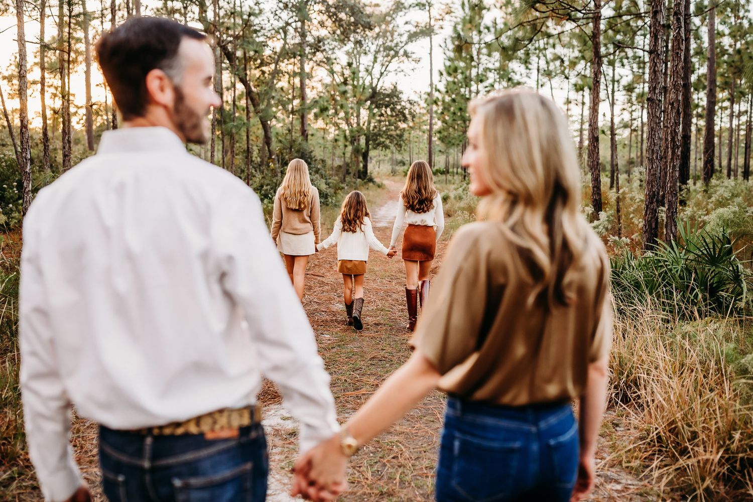 Friends enjoy an outdoor party in a pine forest with wine glasses at golden hour.