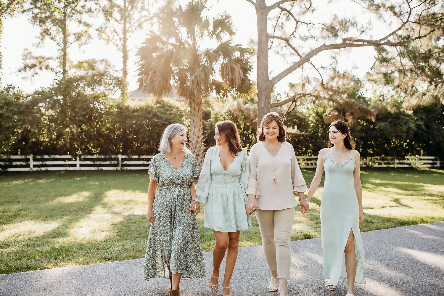 A group walks along a sunlit path outdoors wearing coordinated light-colored dresses and attire.