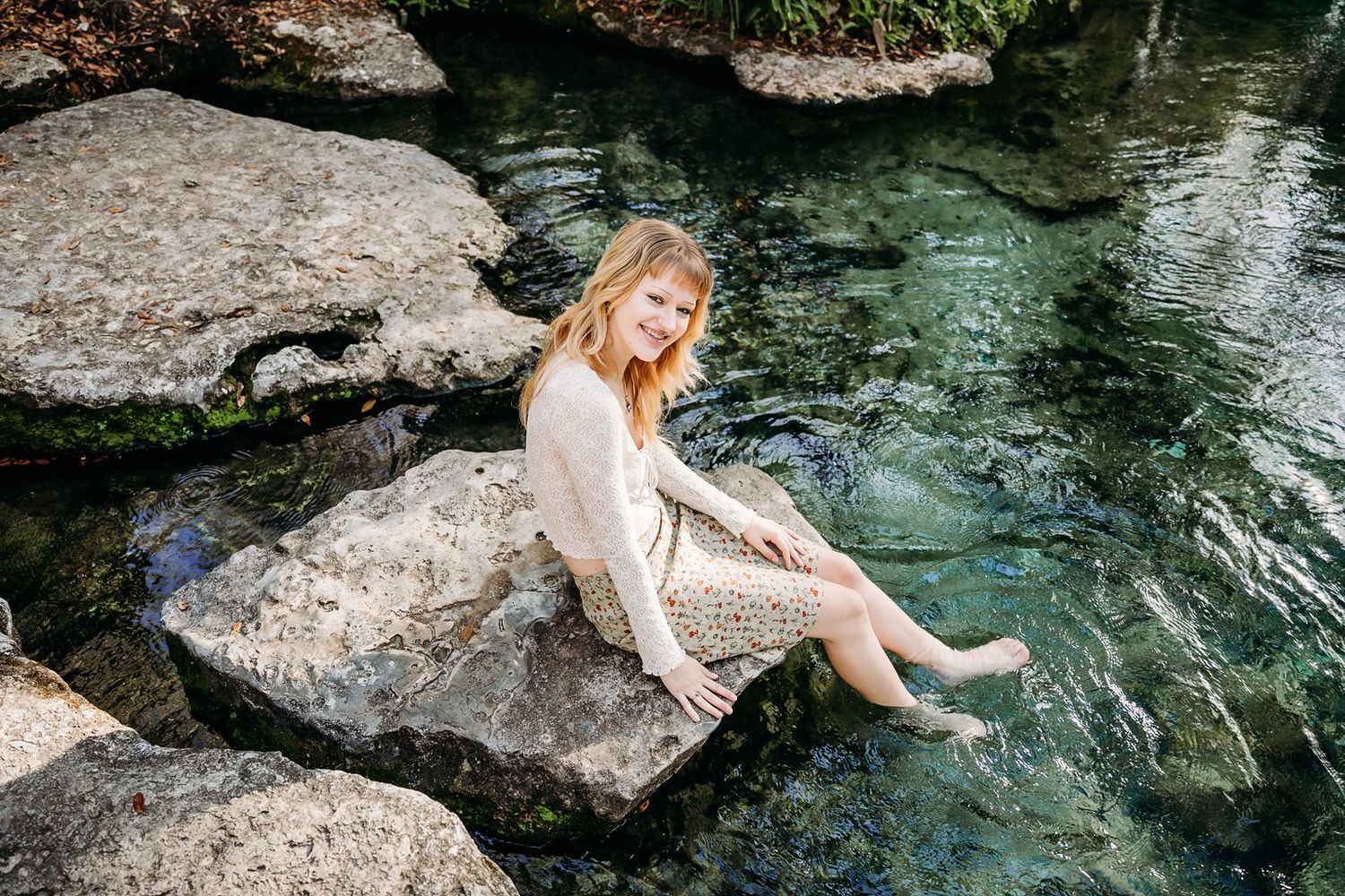 Model poses gracefully by crystal clear turquoise water among large rocks in a natural setting.
