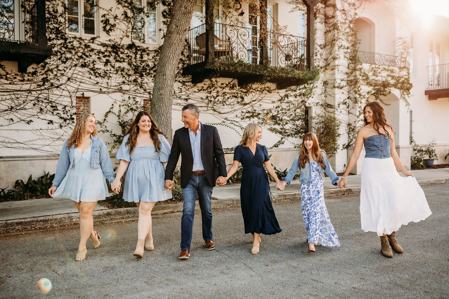 Group of people walk along a stone wall wearing casual spring attire during golden hour.