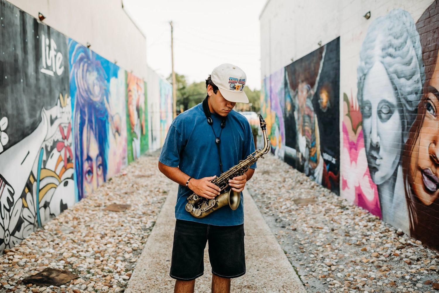 A person in blue stands along a colorful graffiti wall with stones scattered on the ground during a photoshoot.