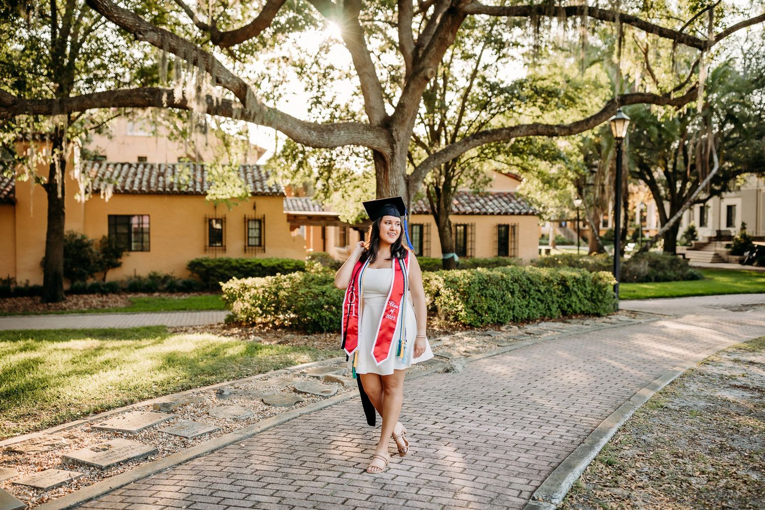 A walkway lined with Spanish moss-draped oak trees leads through a historic Southern estate on a sunny day.