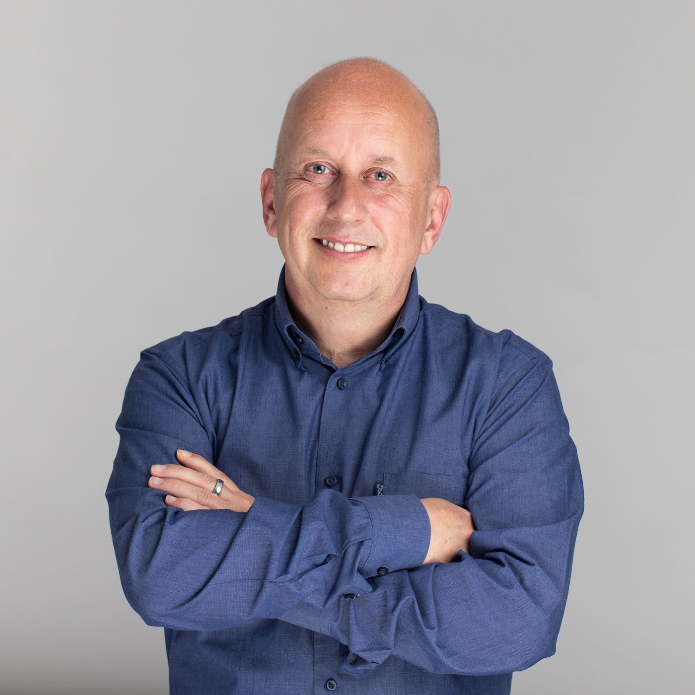 Person in navy blue button-down shirt standing with arms crossed against gray background.