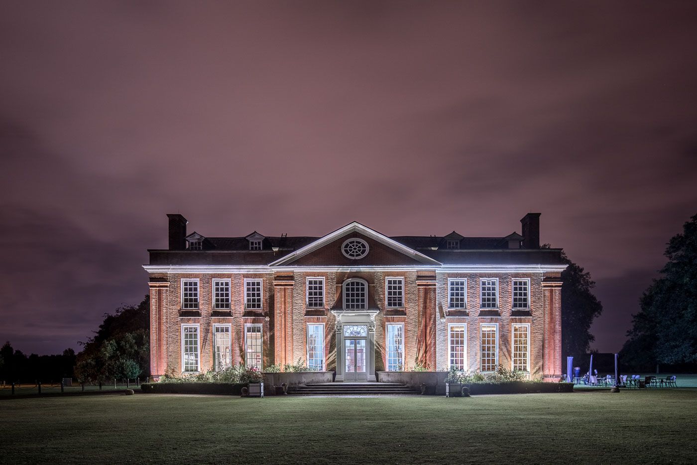 A stately Georgian mansion illuminated at night with warm lighting against a dramatic purple sky.