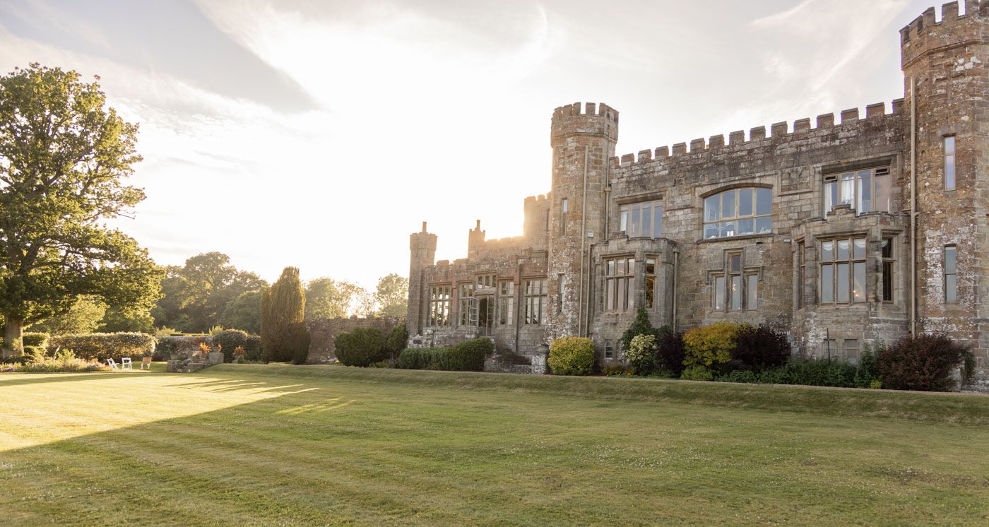 Sunlight illuminates the historic stone castle with towers and crenellated walls across a manicured green lawn.