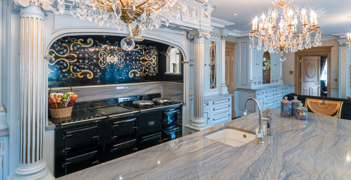 Luxury kitchen interior with black range cooker, crystal chandeliers, and ornate white mouldings against marble floors.