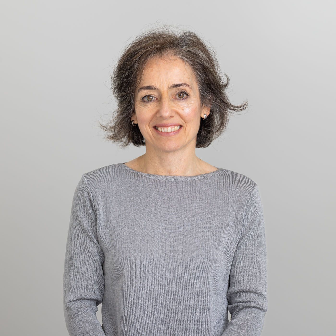Portrait photo of a person with short grey hair wearing a grey long-sleeved top against a light background.