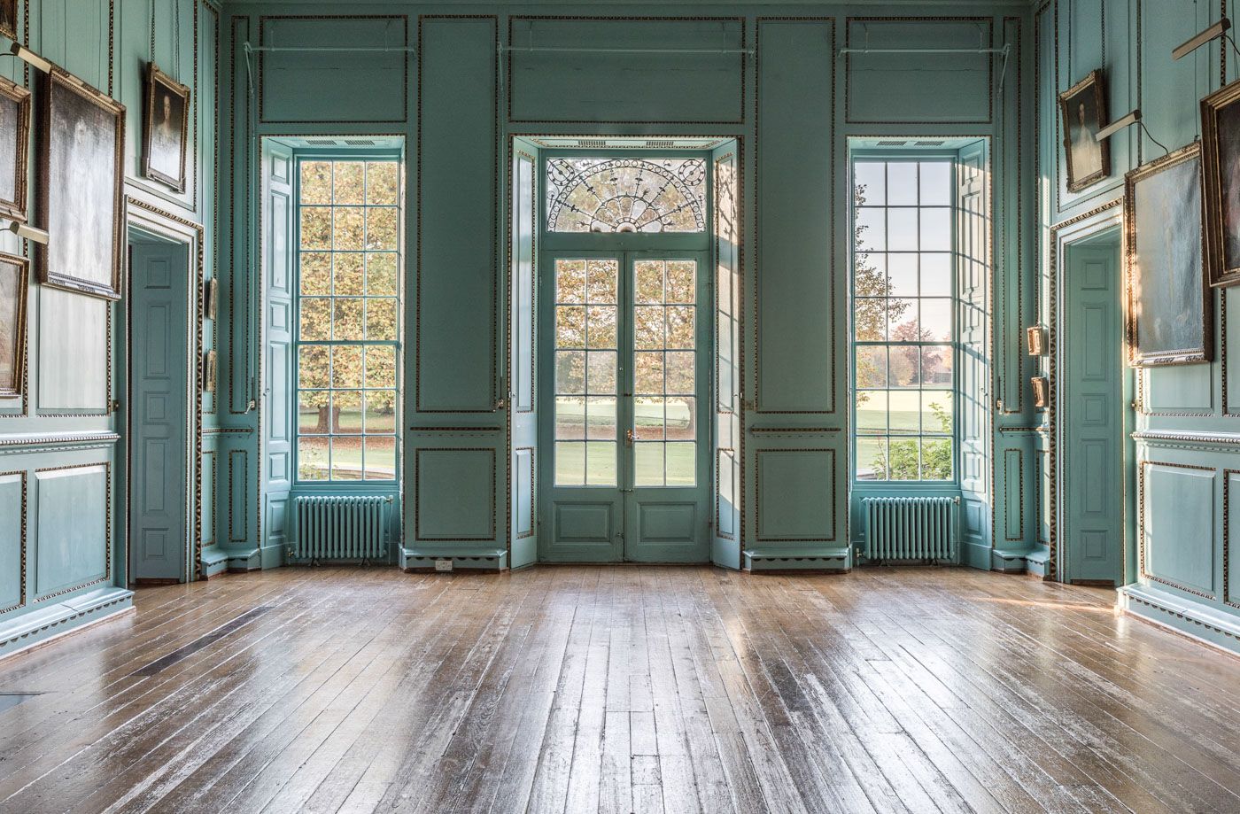 Elegant mint green historic room interior with tall windows, wooden floors and ornate wall paneling in period style.