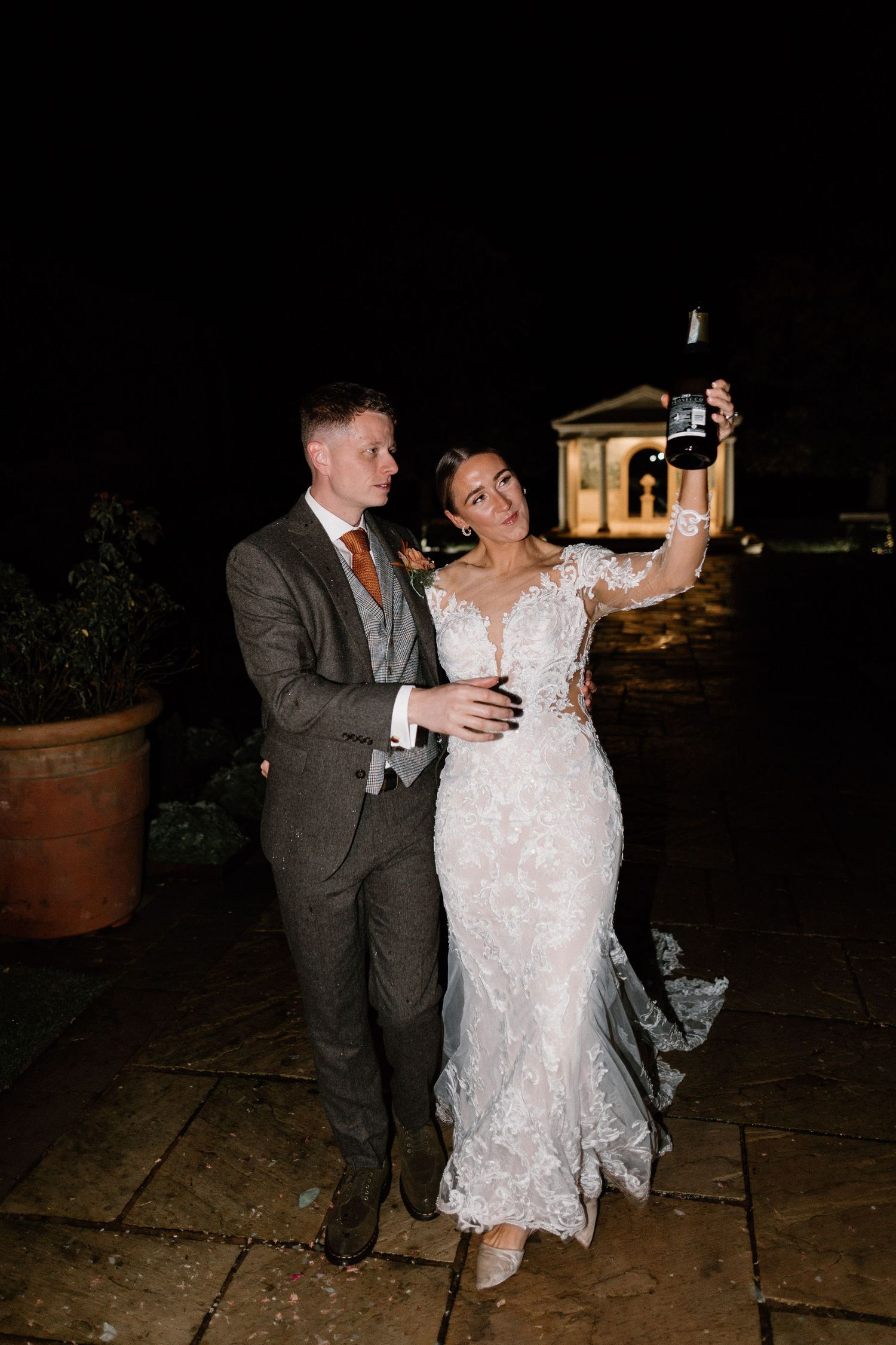 Bride and groom celebrating at night, bride holding a camera aloft outdoors.