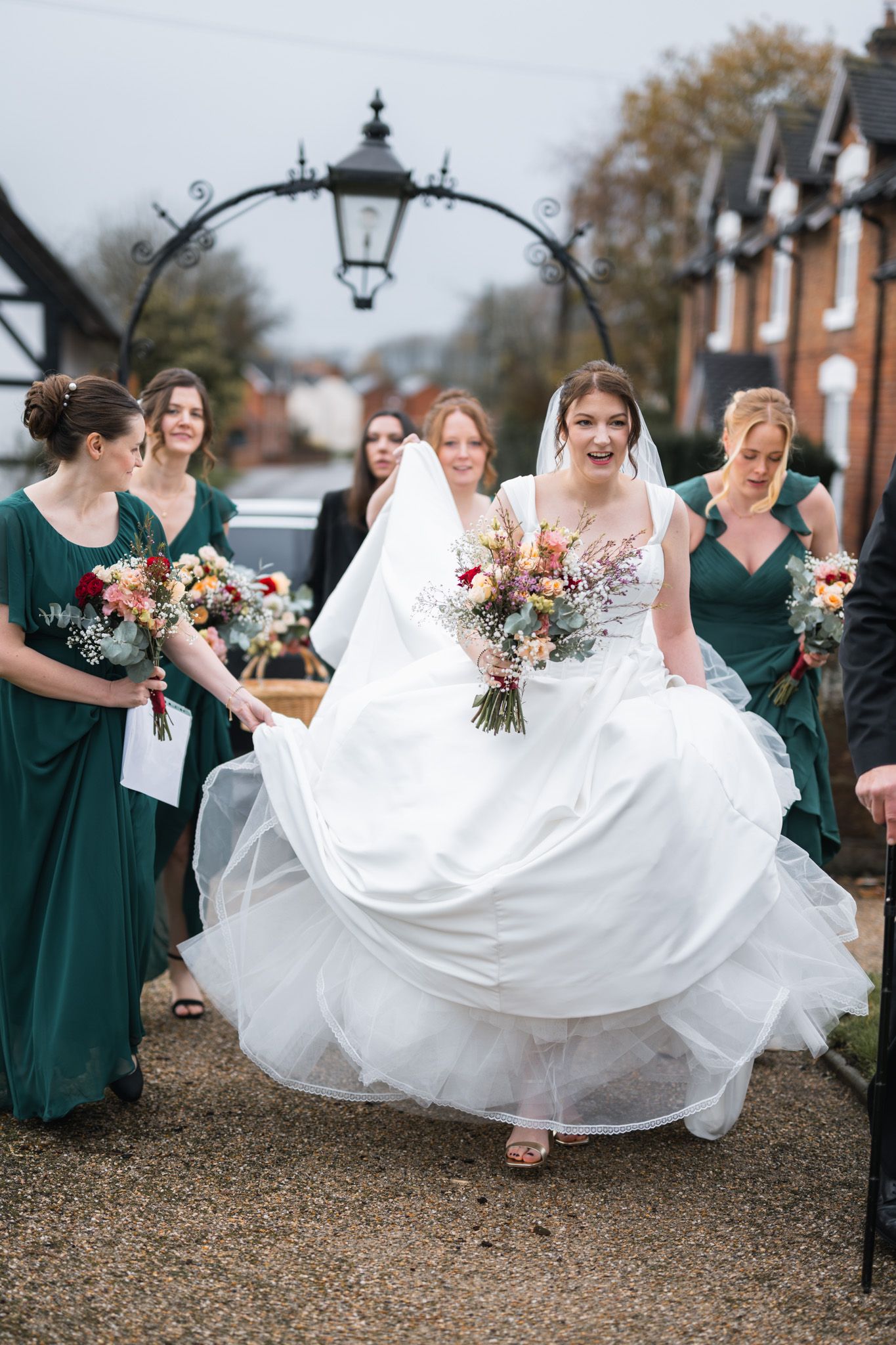 Bride in full white ballgown with colorful bouquet walking with bridesmaids in emerald green dresses.