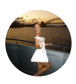 Woman in white dress posing on a boat at sunset with Sydney Harbour Bridge in the background.