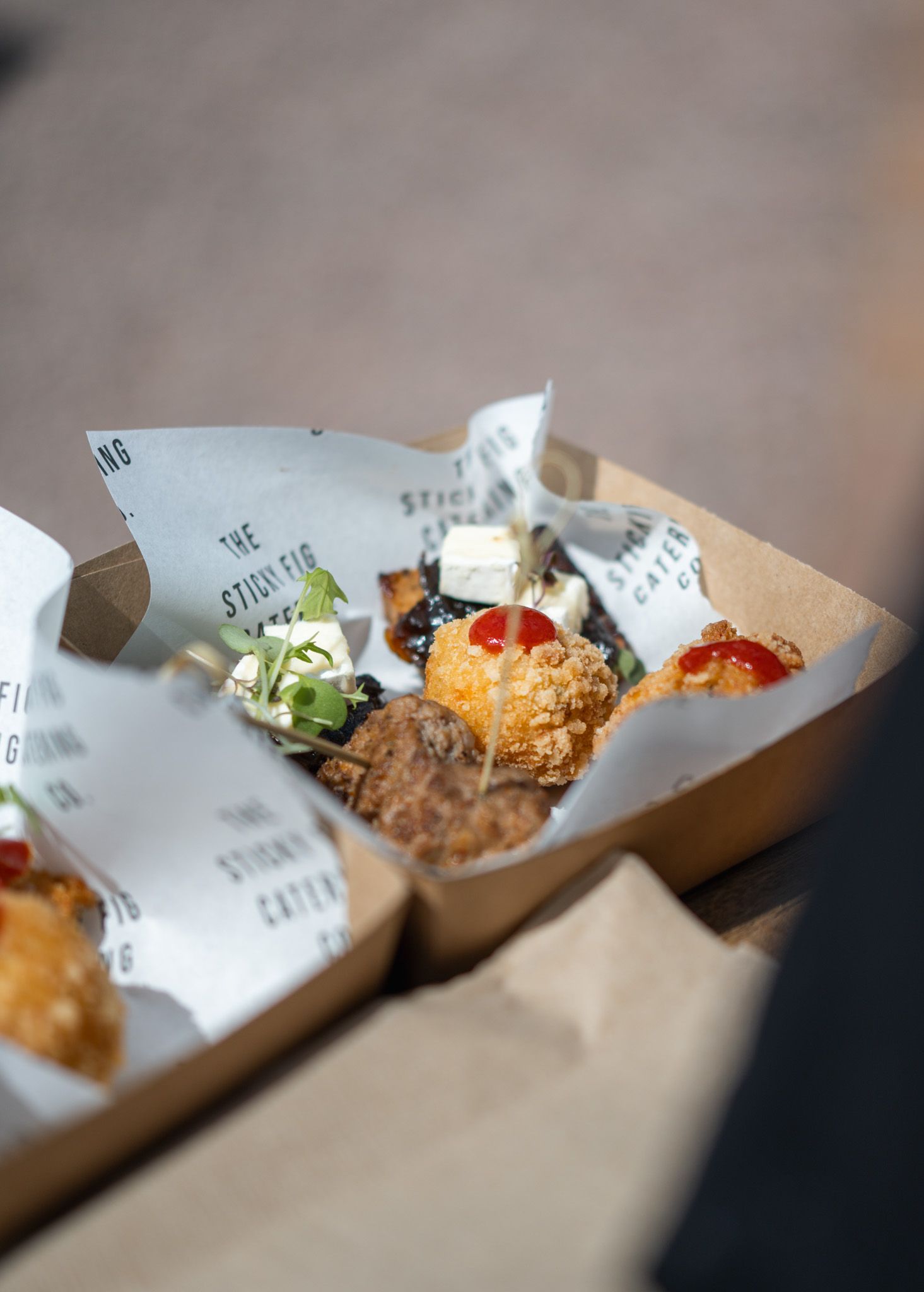 Takeaway cardboard box filled with gourmet street food bites, wrapped in branded paper from The Stinking Catering Co.