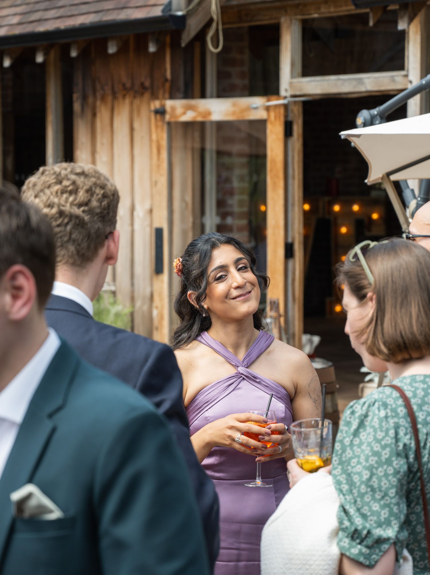 Woman in purple halter dress smiling and holding a cocktail at an outdoor wedding reception.