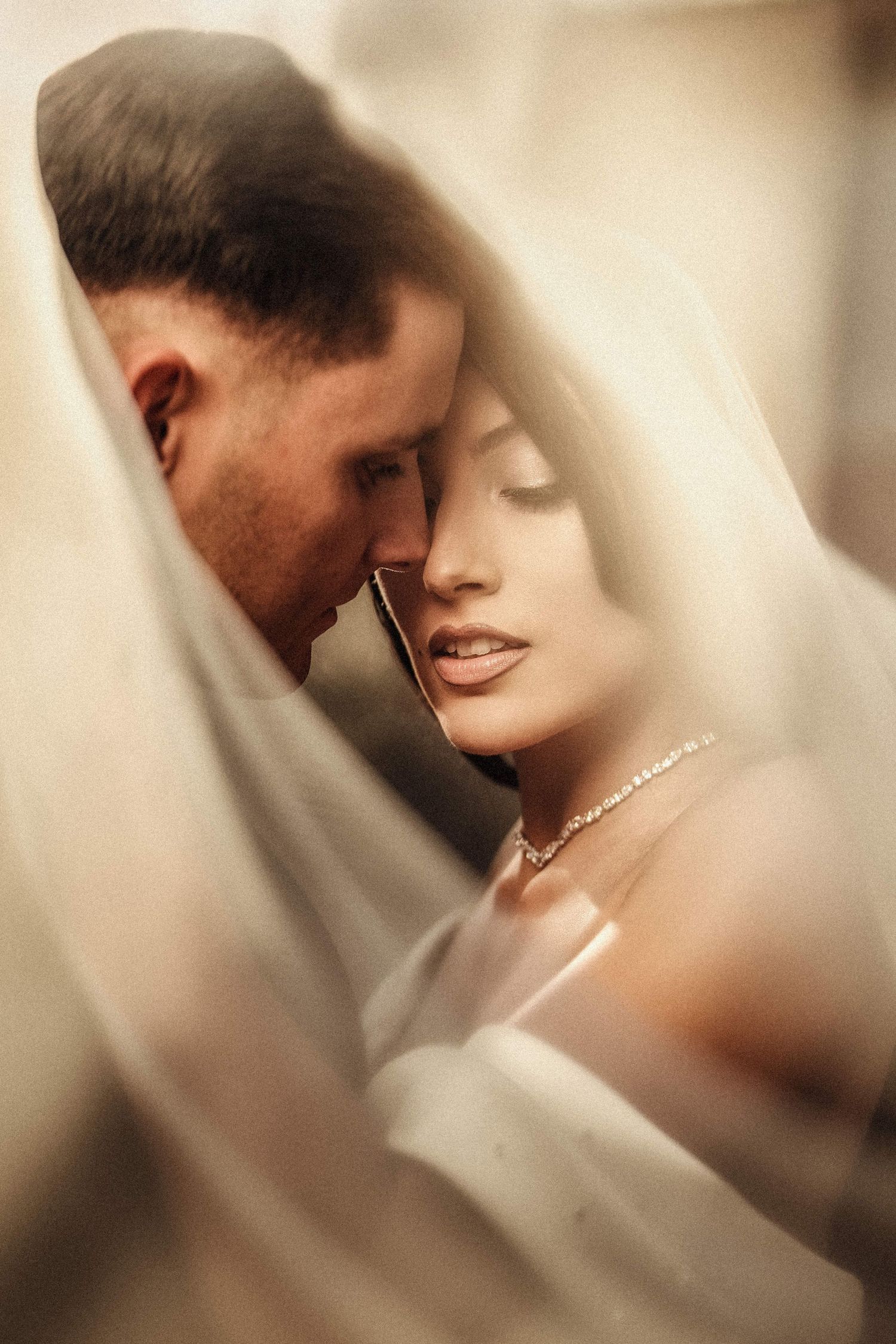 Intimate artistic portrait through sheer fabric with soft focus and warm tones.