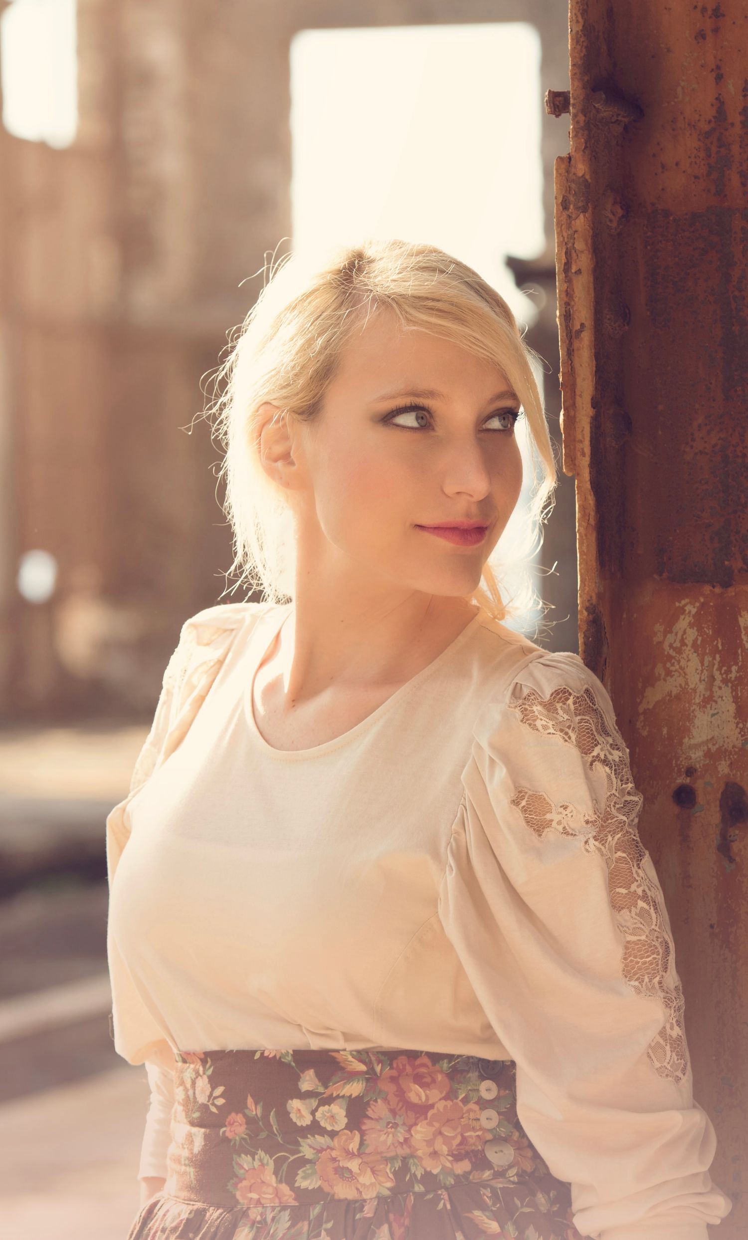 Woman in vintage-inspired cream blouse poses artistically in soft lighting.