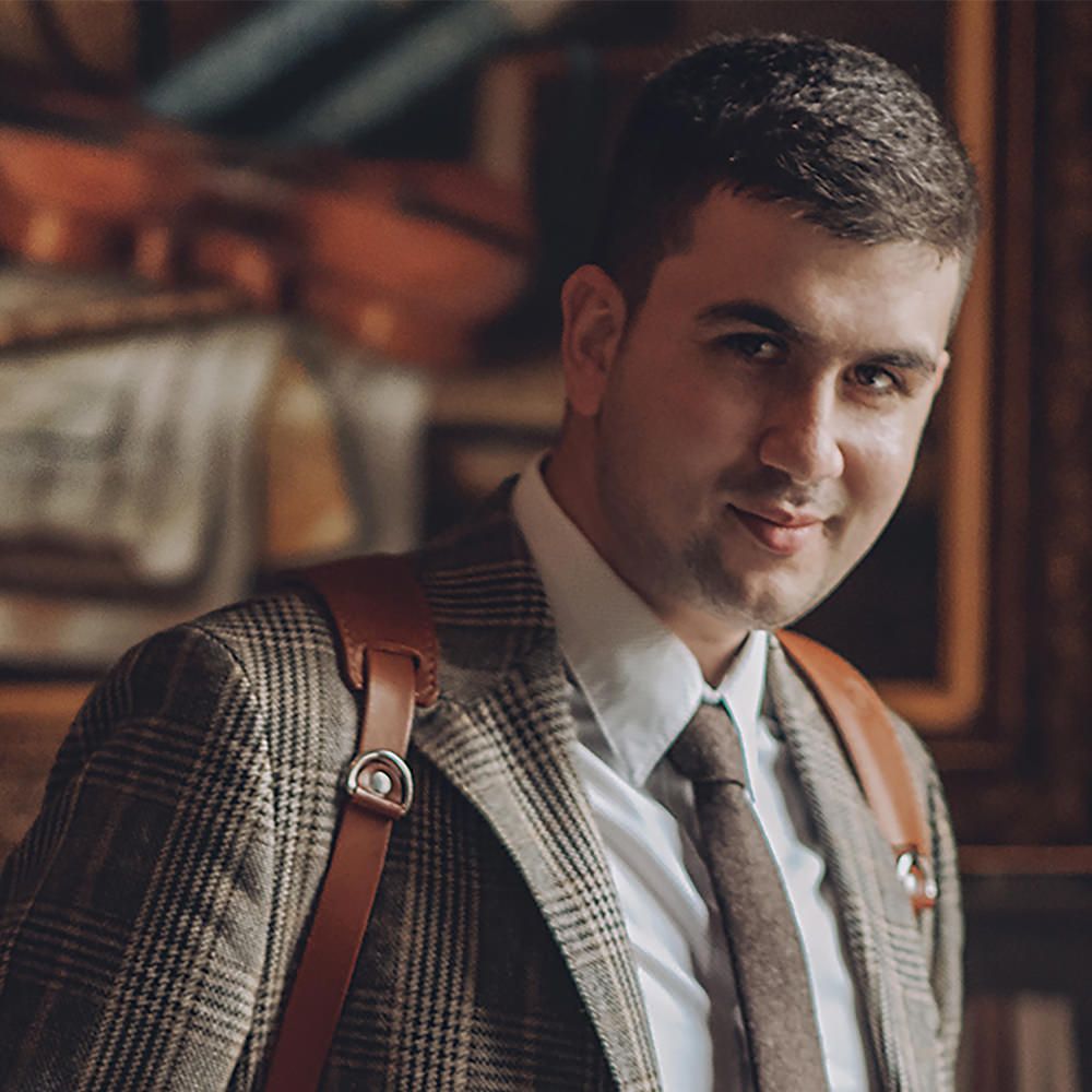 Professional wearing plaid blazer and leather camera strap smiles while indoors.