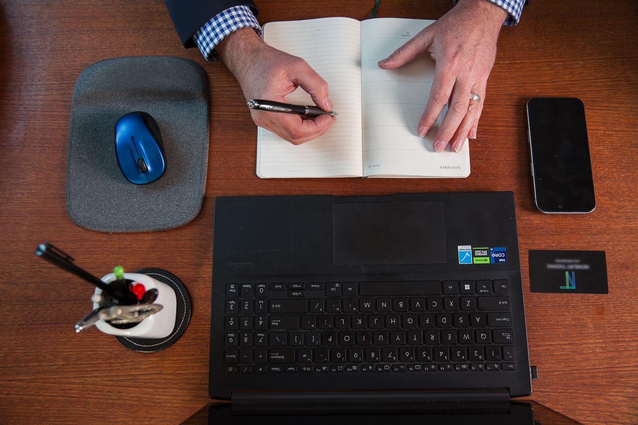 Person typing on a wireless keyboard at a wooden desk with a computer mouse and smartphone nearby.