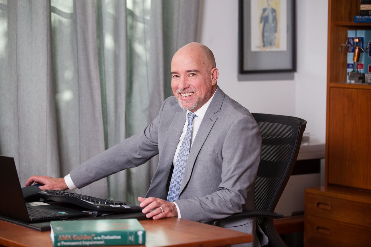 Professional in a gray suit works at a modern office desk with bookshelves and window light.